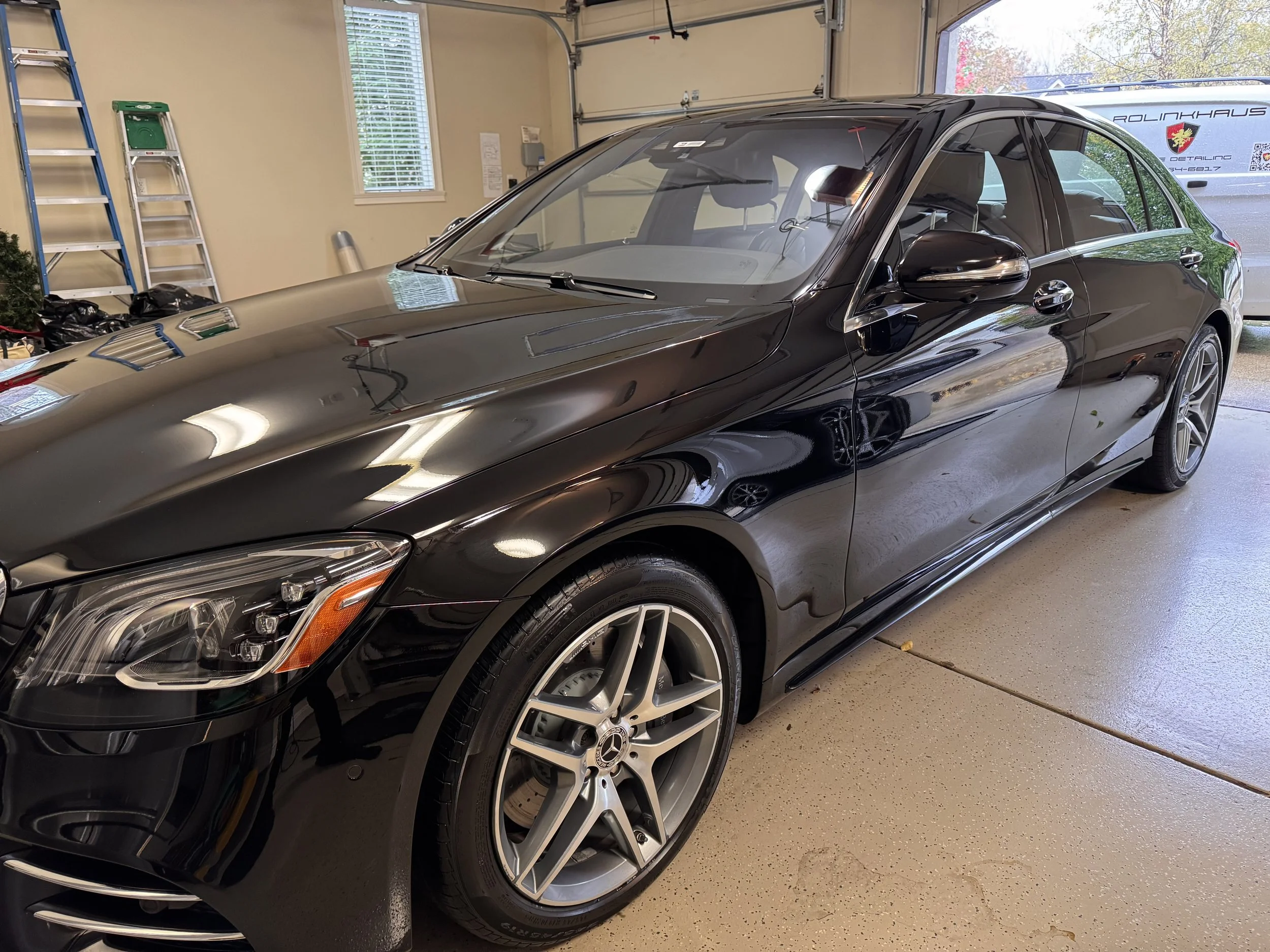 A black luxury sedan parked inside a garage with a polished exterior, alloy wheels, and tinted windows.