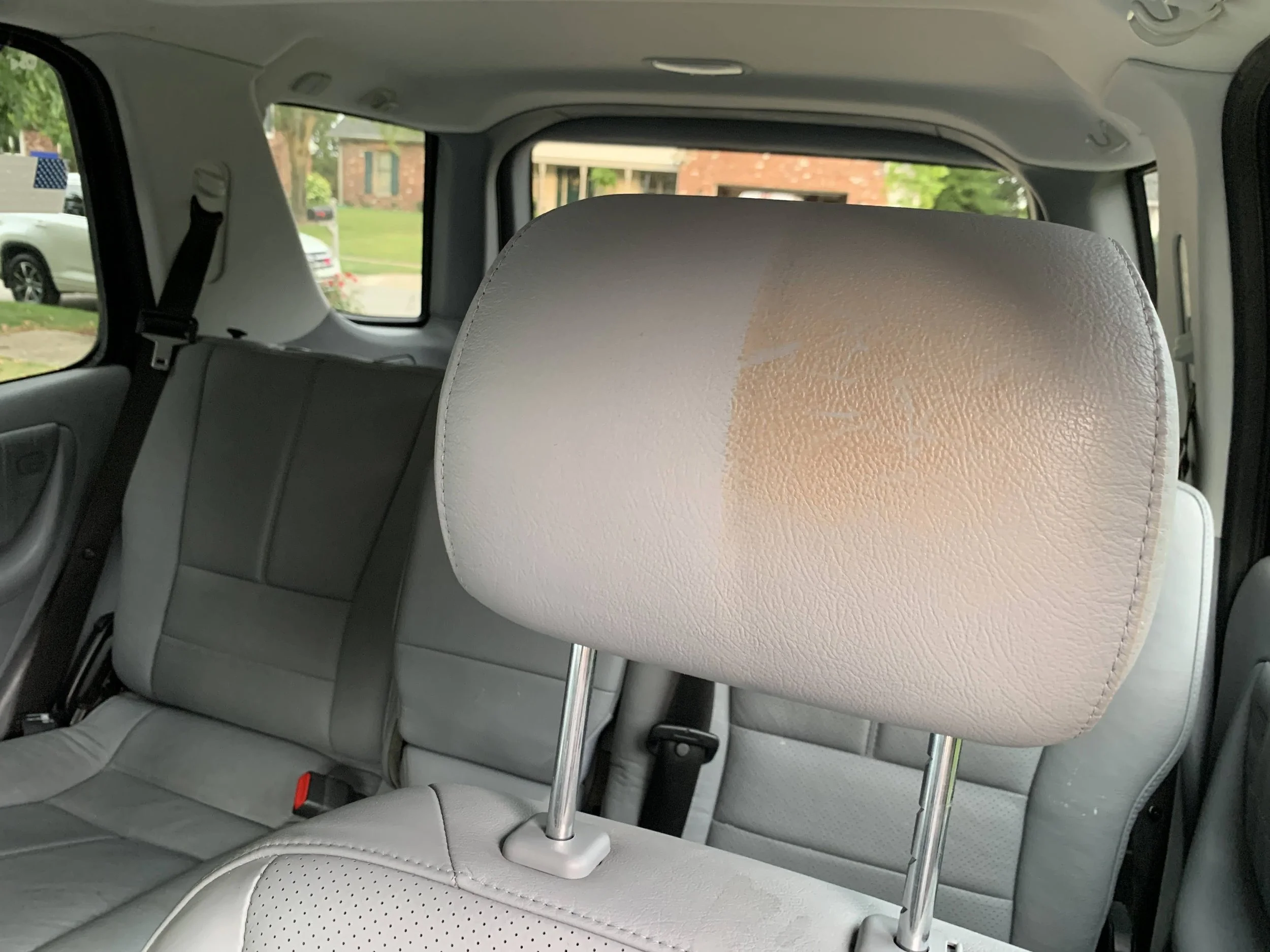 Interior of a vehicle showing a beige headrest with a faded or stained area, and gray seats in the back.