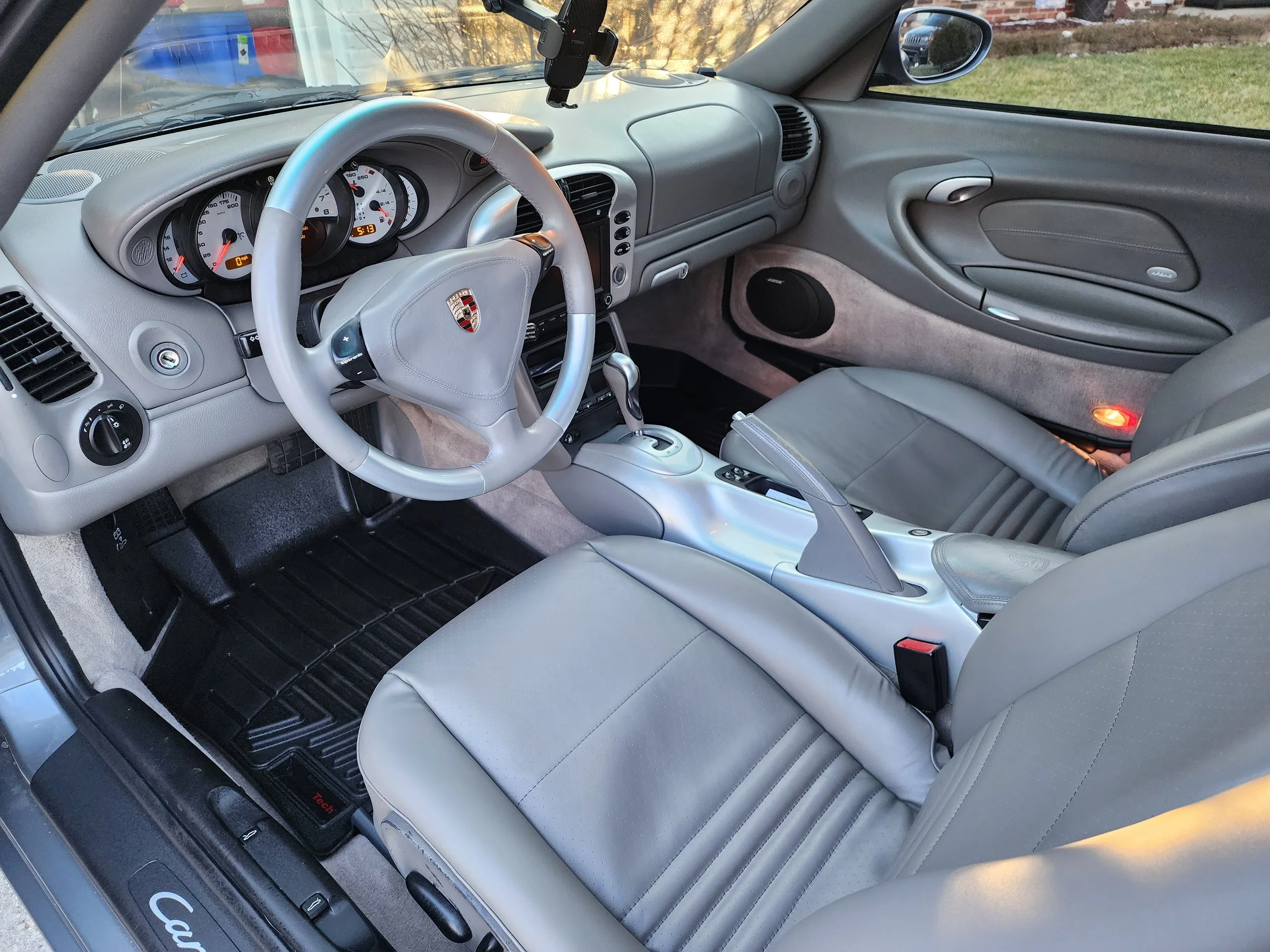 Interior of a silver Porsche sports car, showing the dashboard, steering wheel, center console, and leather seats in beige.