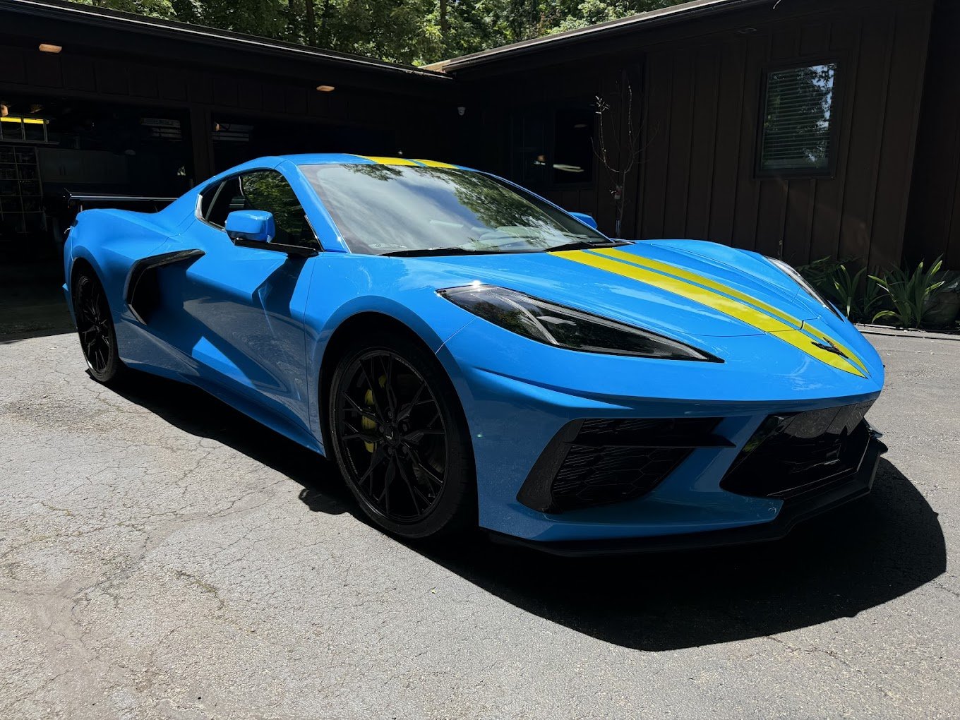 Blue sports car parked outdoors with yellow racing stripes on the hood and roof.