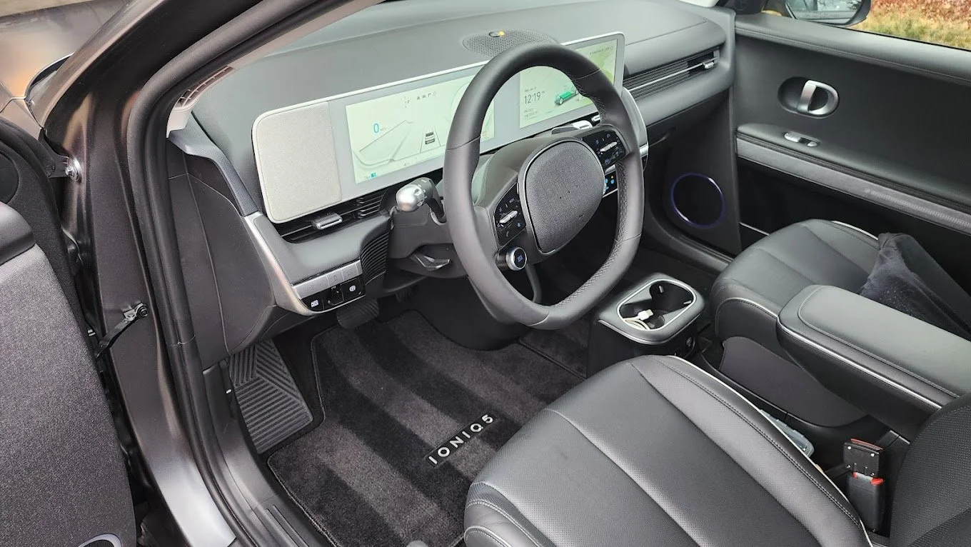 Interior of a modern car showing a digital dashboard, steering wheel, center console, and front seats with a black and gray color scheme.