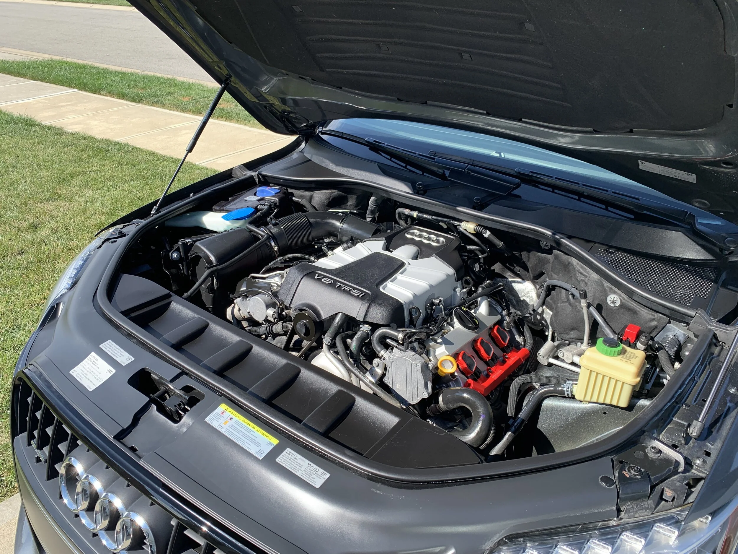 Engine of an Audi car with visible V6 TFSI badge, open hood showing engine components, hoses, and fluid reservoirs.