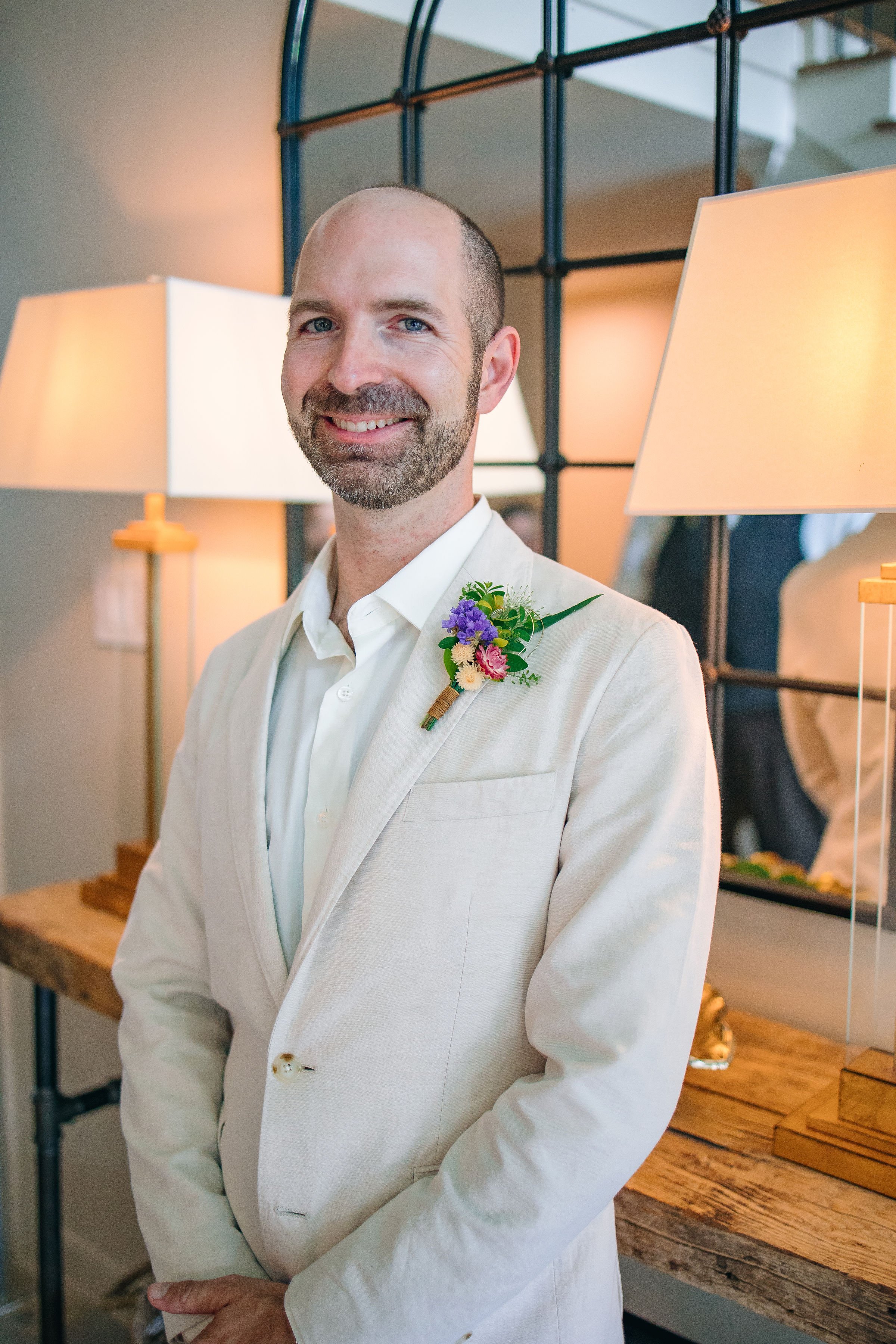 Groom in cream linen suit with purple, white, and pink boutonniere featuring violin strings. Flowers by Plano, Texas florist Terra Cotta Blooms. Photo by Radiant Film &amp; Photo.