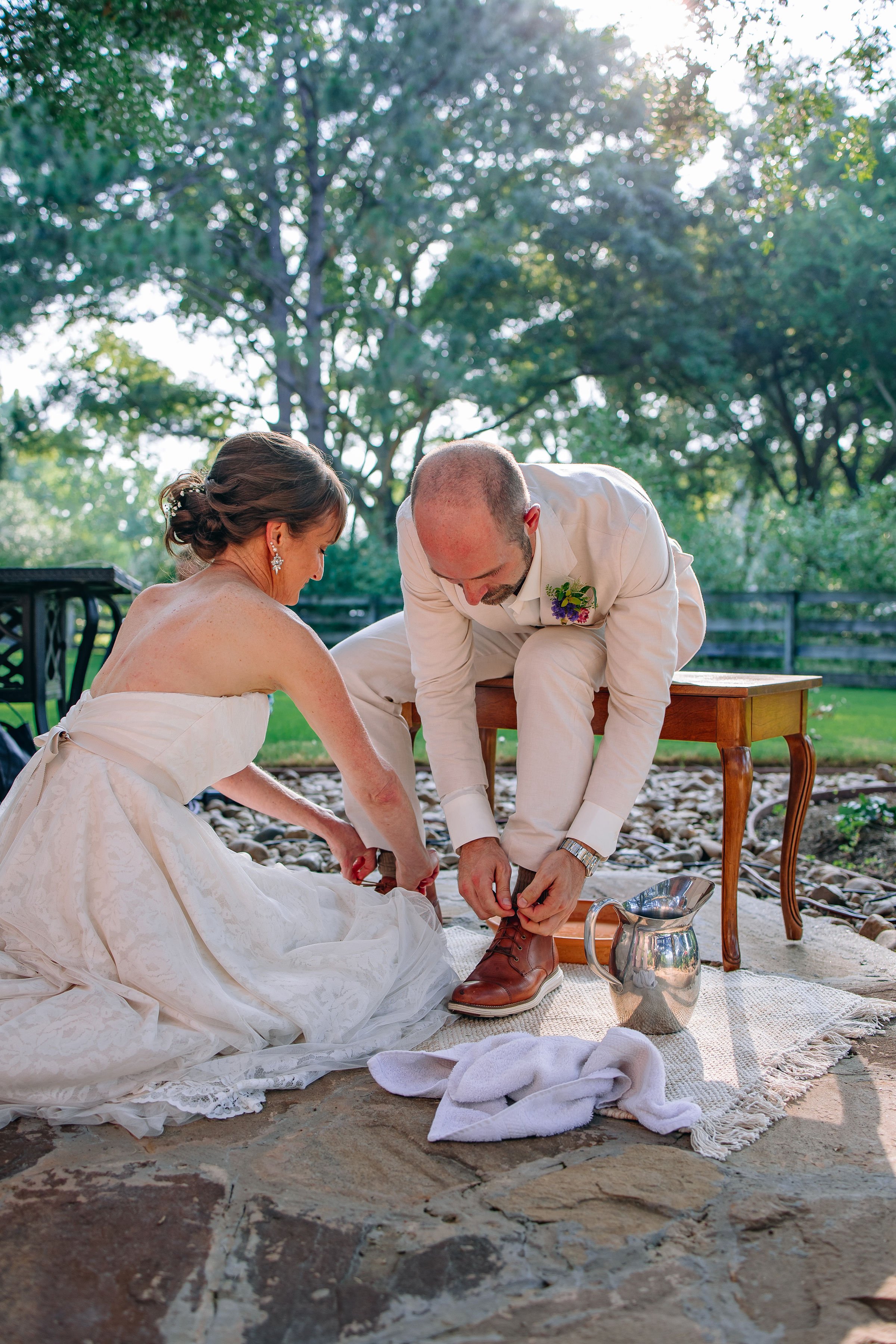 Bride washing groom's feet at an outdoor backyard wedding. Flowers by Plano, Texas florist Terra Cotta Blooms. Photo by Radiant Film &amp; Photo.