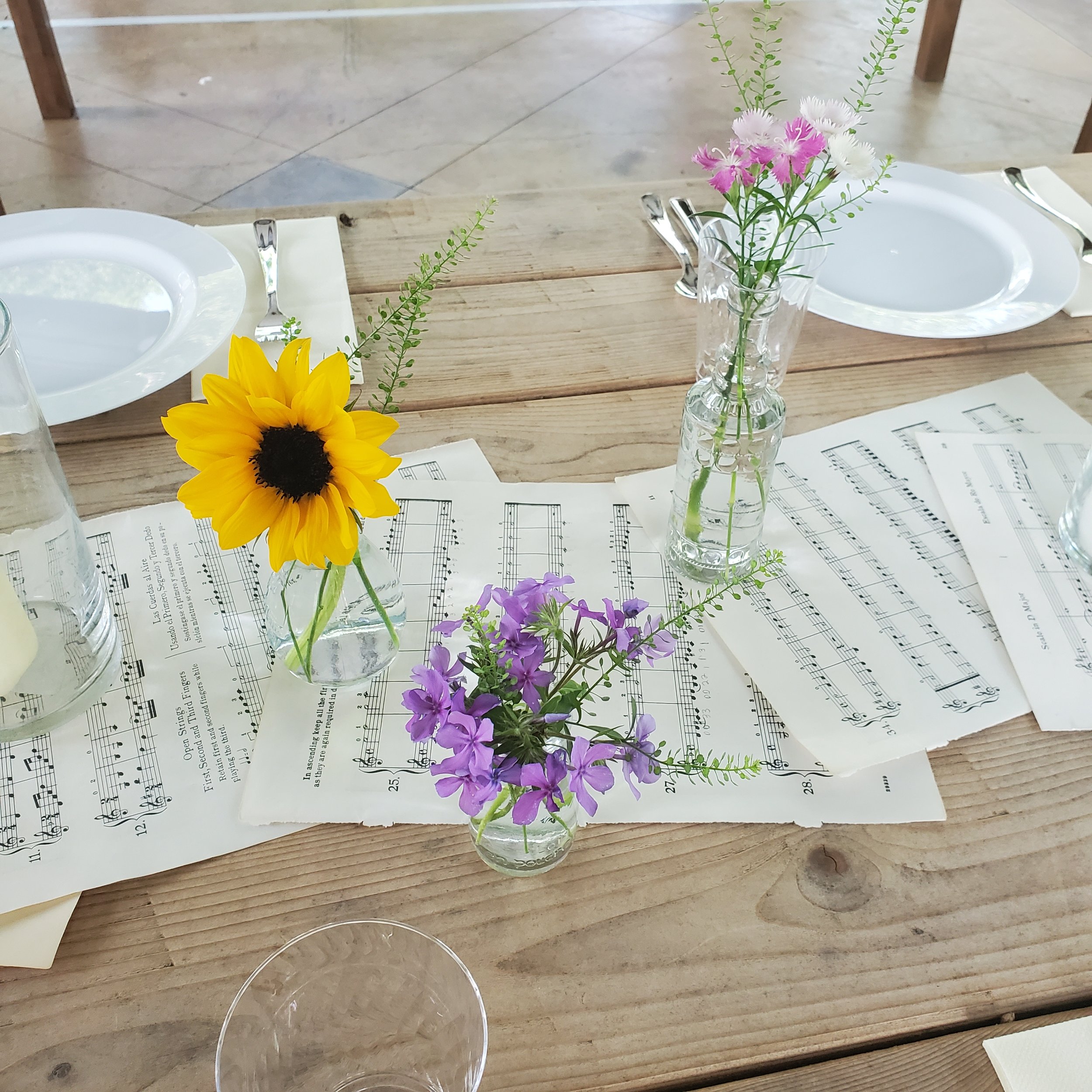 Bud vases on reception table with sheet music runner at an outdoor wedding. Flowers by Plano, Texas florist Terra Cotta Blooms. Photo by Radiant Film &amp; Photo.