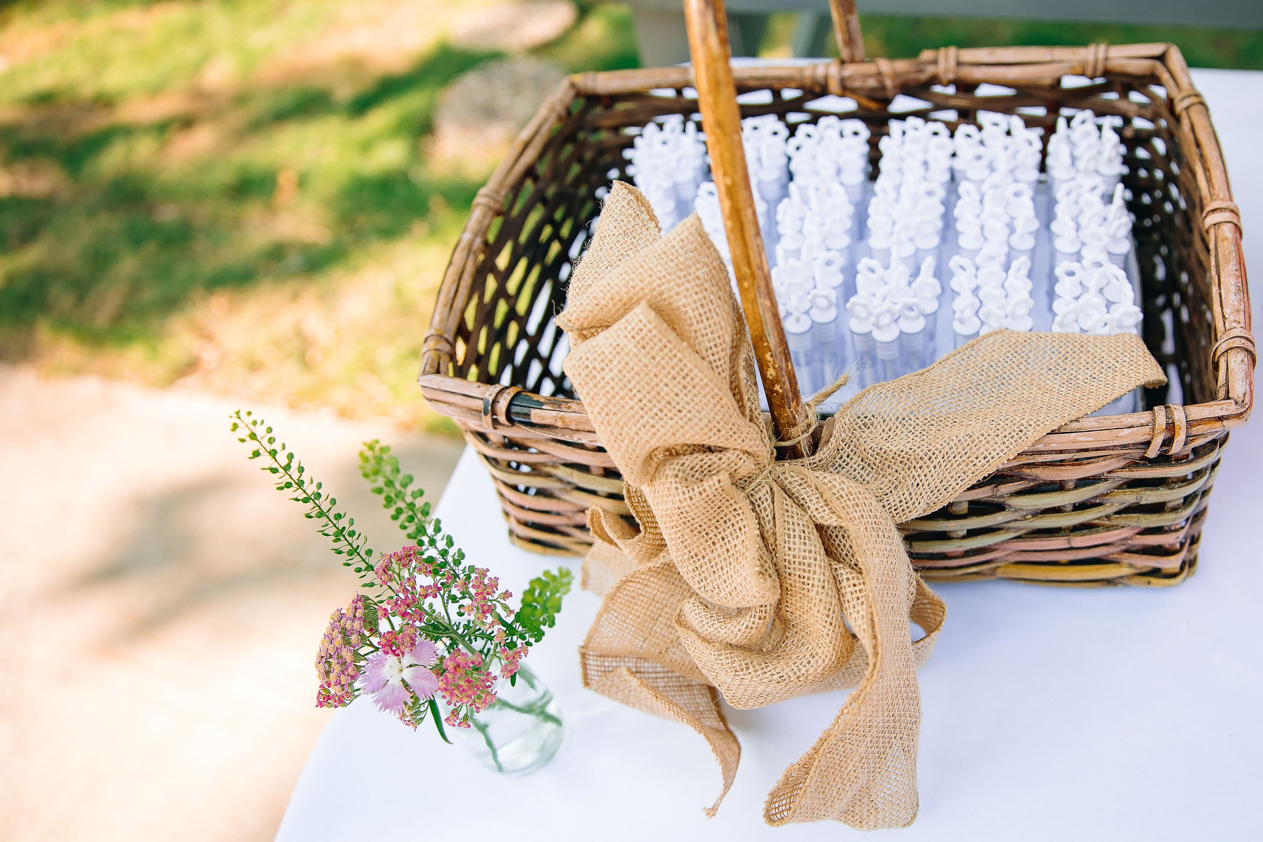 Bud vases and wicker basket of bubbles with burlap ribbon bow for an outdoor backyard wedding. Flowers by Plano, TX florist Terra Cotta Blooms. Photo by Radiant Film &amp; Photo.