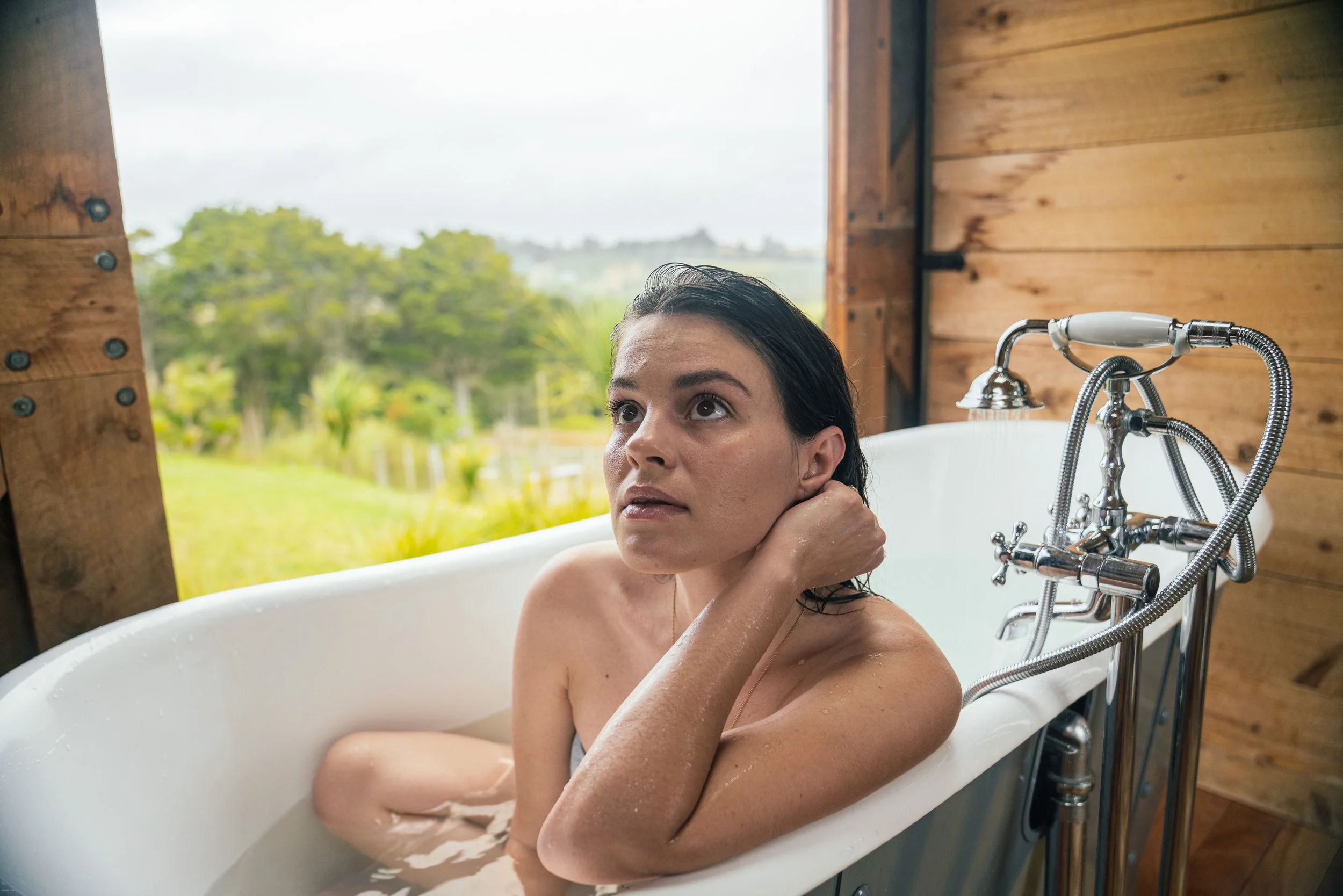 Carrie Rad relaxing in an outdoor bathtub at a countryside Airbnb in Mangawhai, Northland, New Zealand, surrounded by the region’s lush rural landscape.