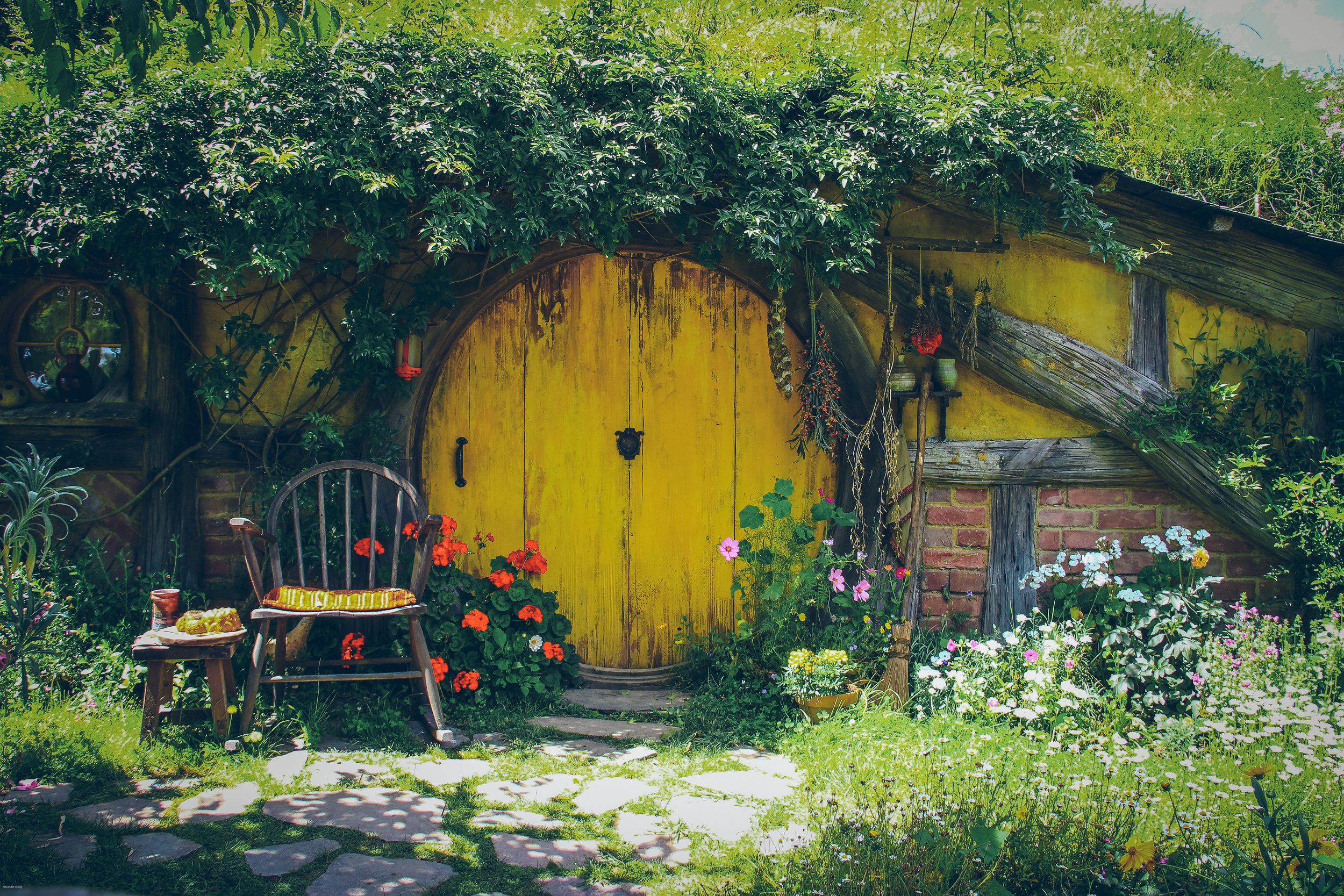 Colorful Hobbit hole with a round yellow door and flower-filled garden at the Hobbiton Movie Set near Matamata, New Zealand.