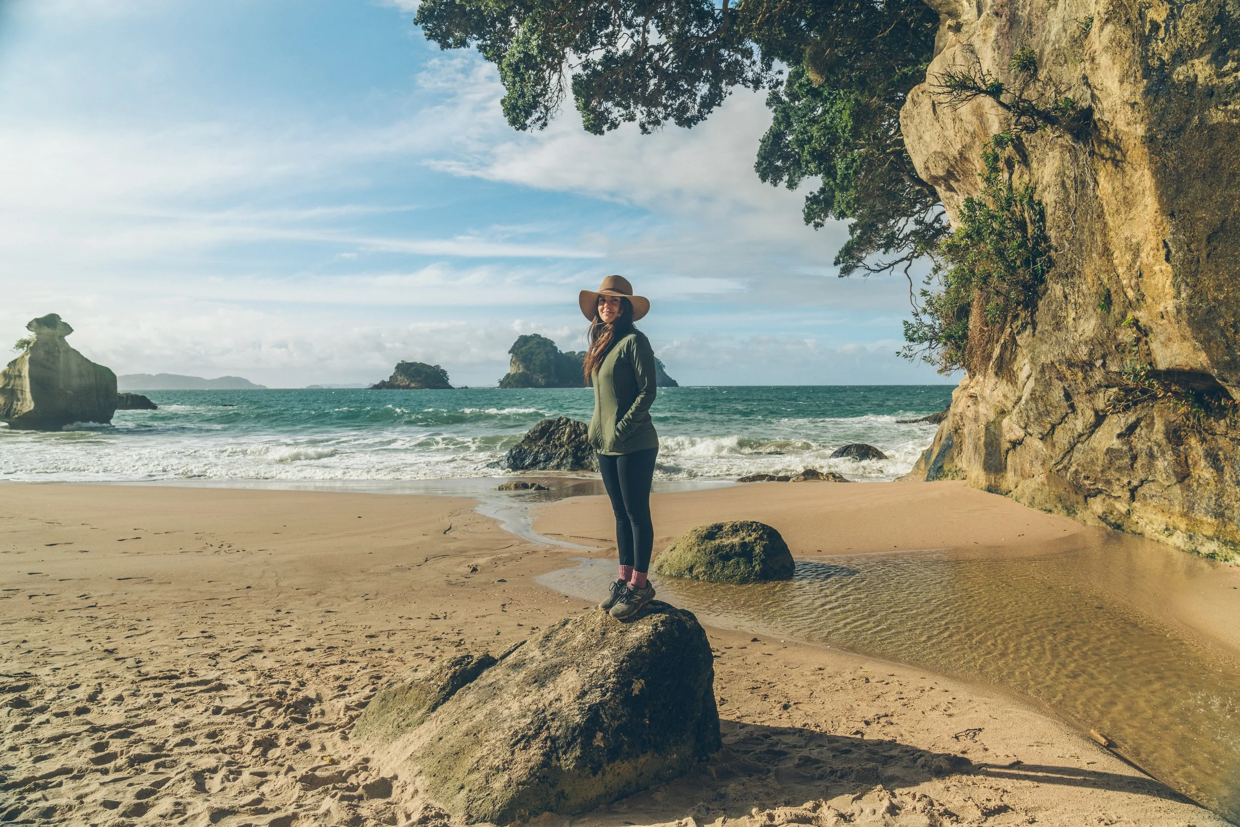 Carrie Rad standing on the beach at Cathedral Cove on the Coromandel Peninsula, North Island, New Zealand, surrounded by dramatic coastal rock formations and turquoise ocean.