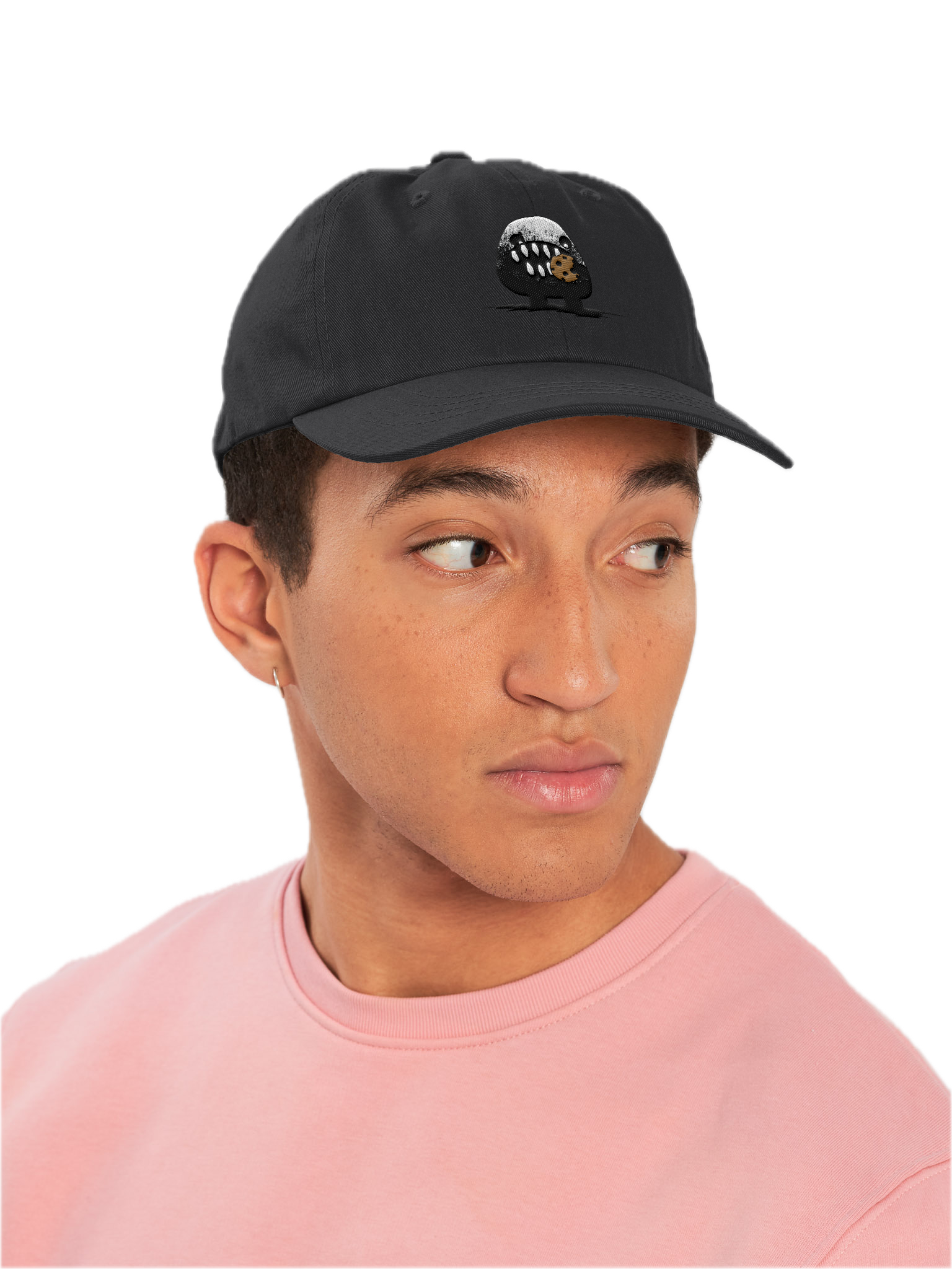 Close-up of a young person with short hair wearing a black baseball cap with a monster design and a light pink shirt, looking to the side.