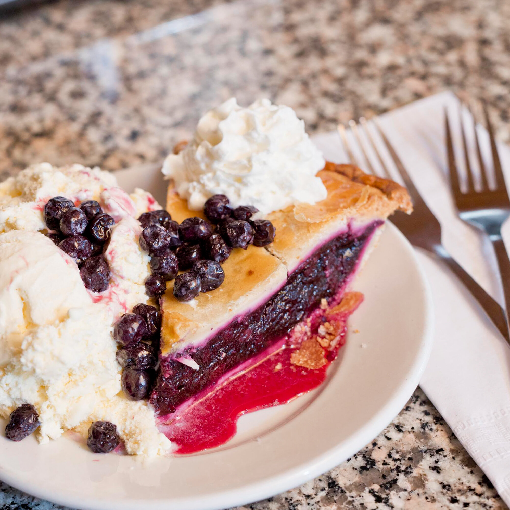  juicy slice of blueberry pie with a heaping side of vanilla ice cream, topped with fresh whipped cream 