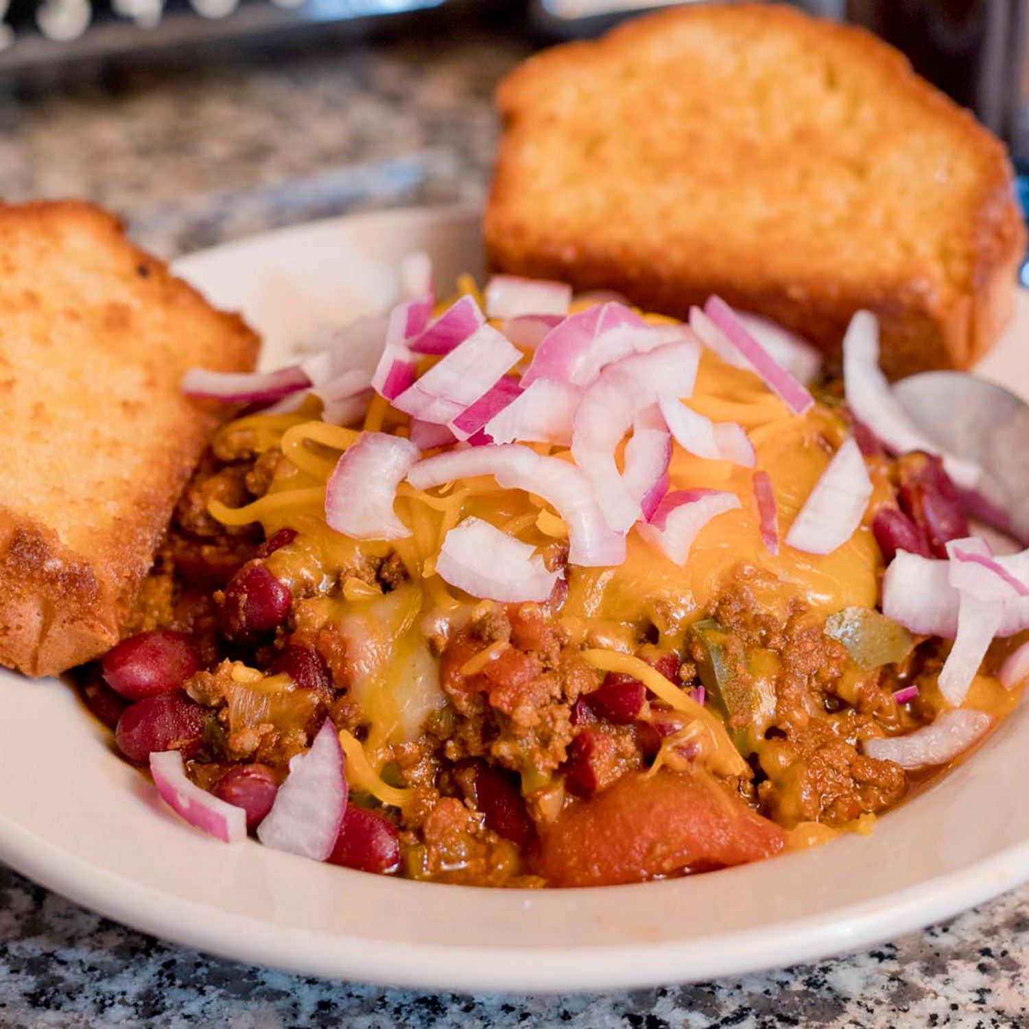  bowl of hearty, hot and savory three bean chili smothered with melted cheese, sliced onions and served with a side grilled corn bread 