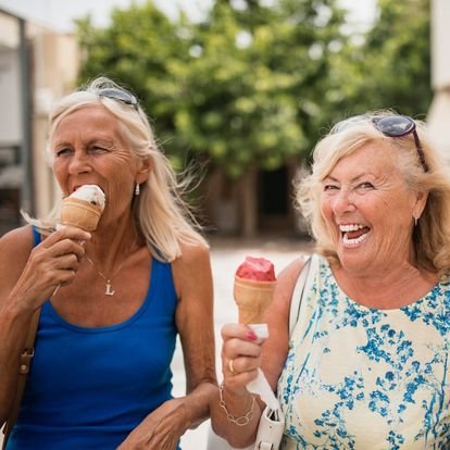  two older women smiling, laughing and each enjoying ice cream cones 