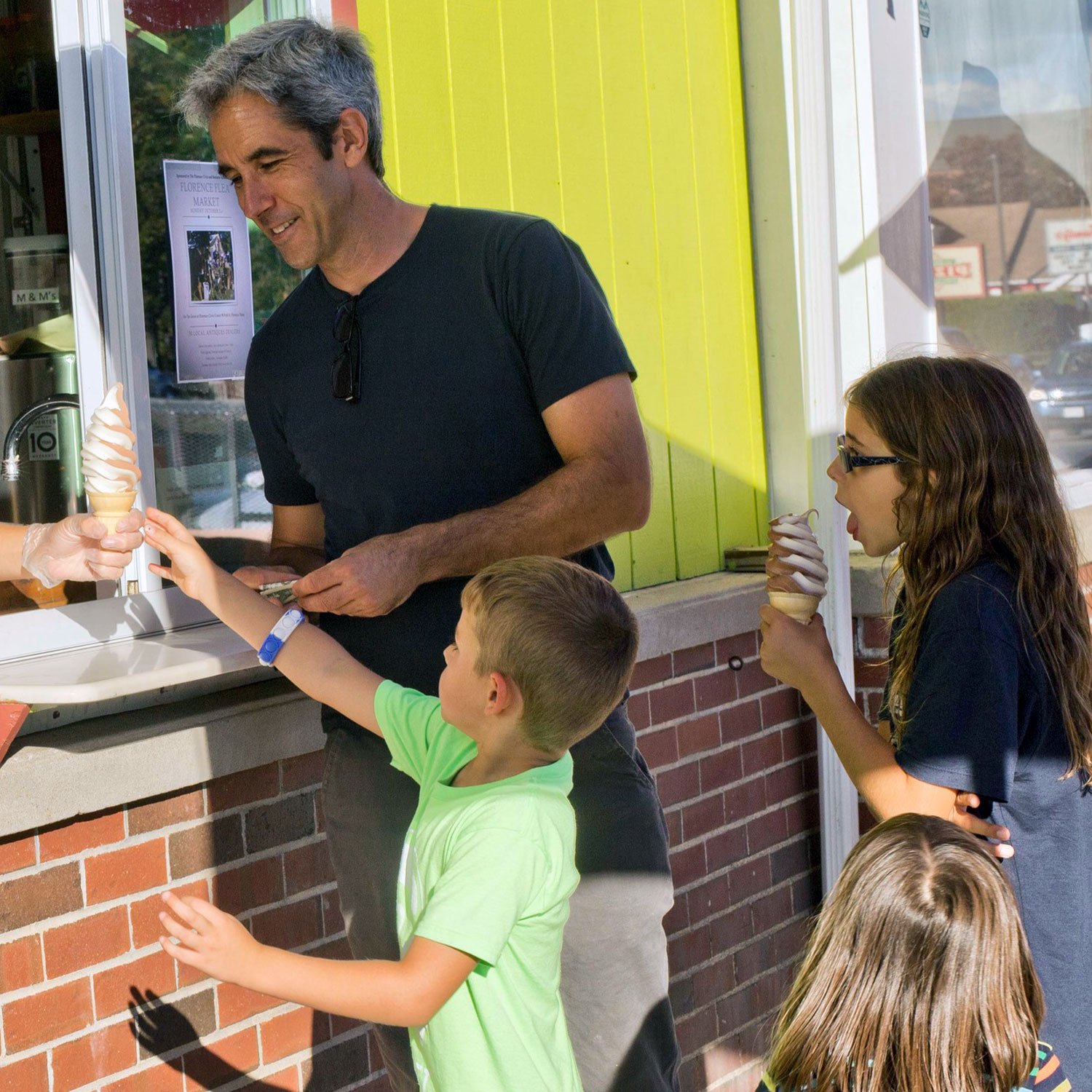  dad in a black t shirt takes his two daughters and son out for ice cream cones on a summer afternoon  