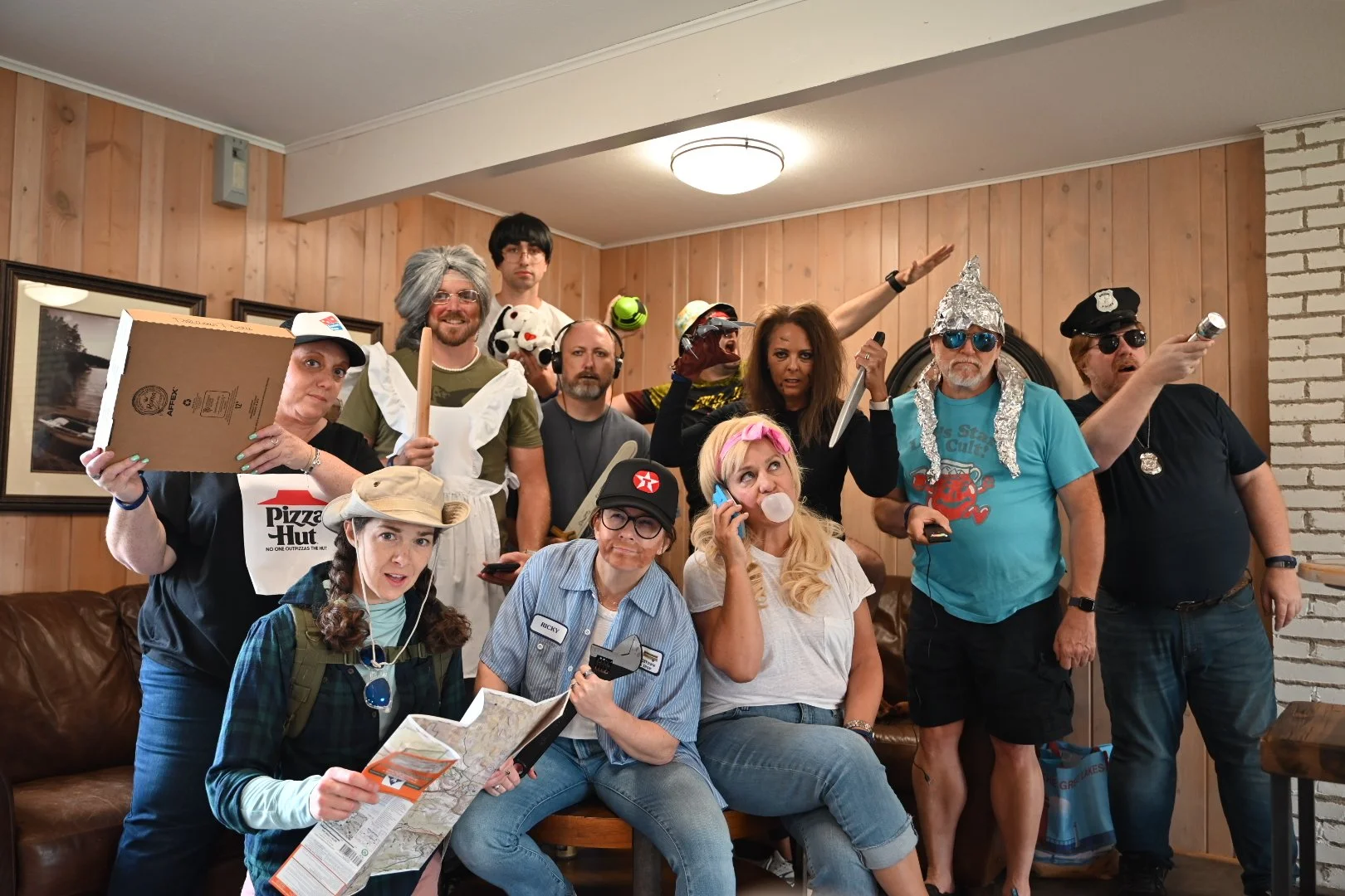 Group of people in humorous and eclectic costumes posing indoors with props.