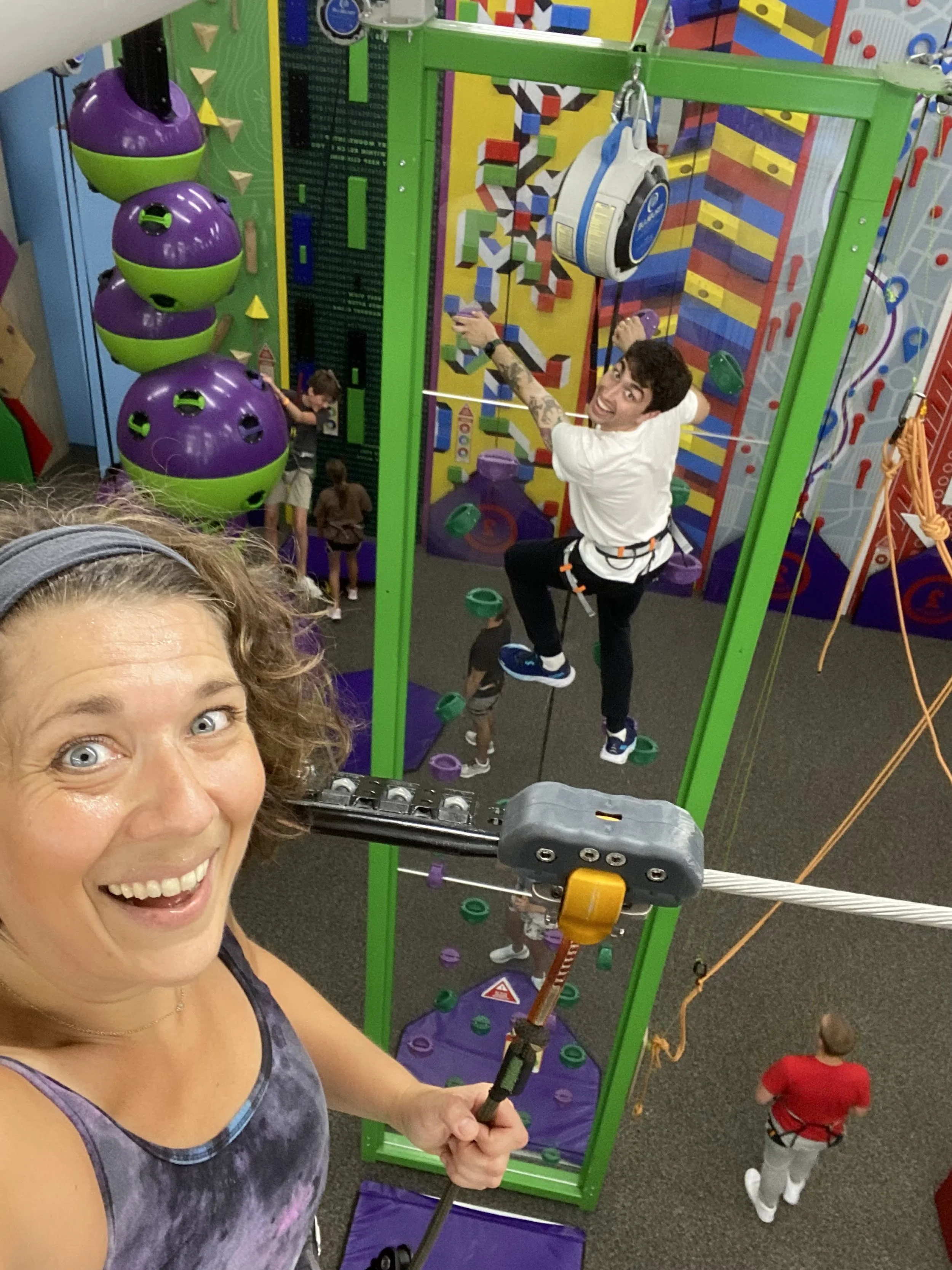 ITG Ignite consumer immersion activity - indoor climbing activity with a person smiling in the foreground and another climbing a colorful wall in the background.