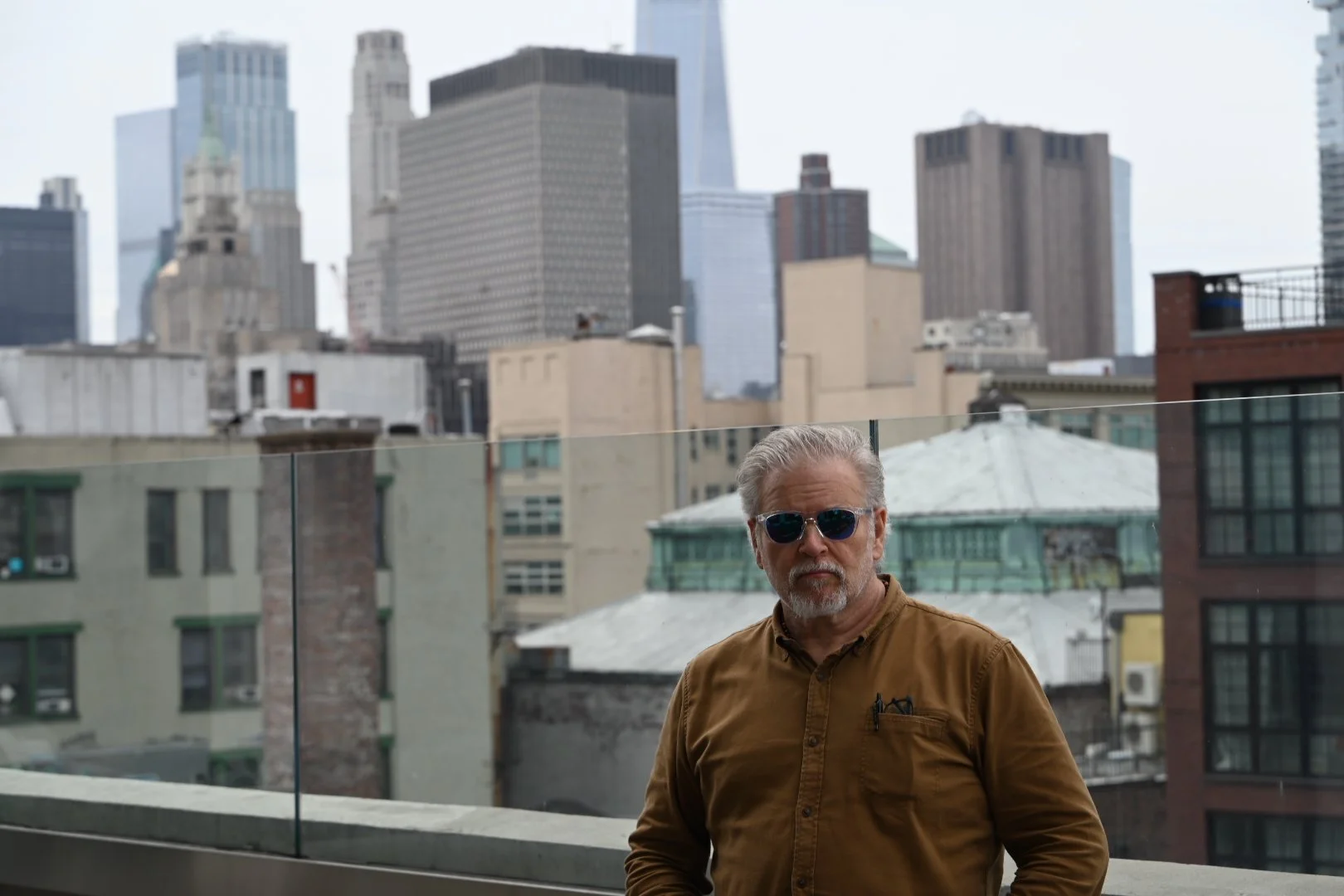 Man with sunglasses stands on a balcony with a city skyline in the background.