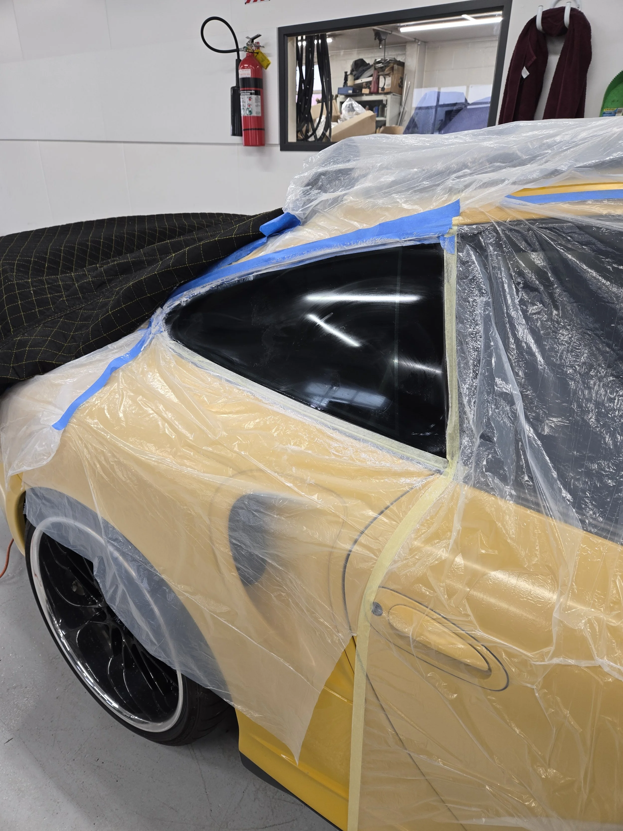 A Porsche GT2 is prepaired for glass stain removal with protective masking applied to surrounding panels