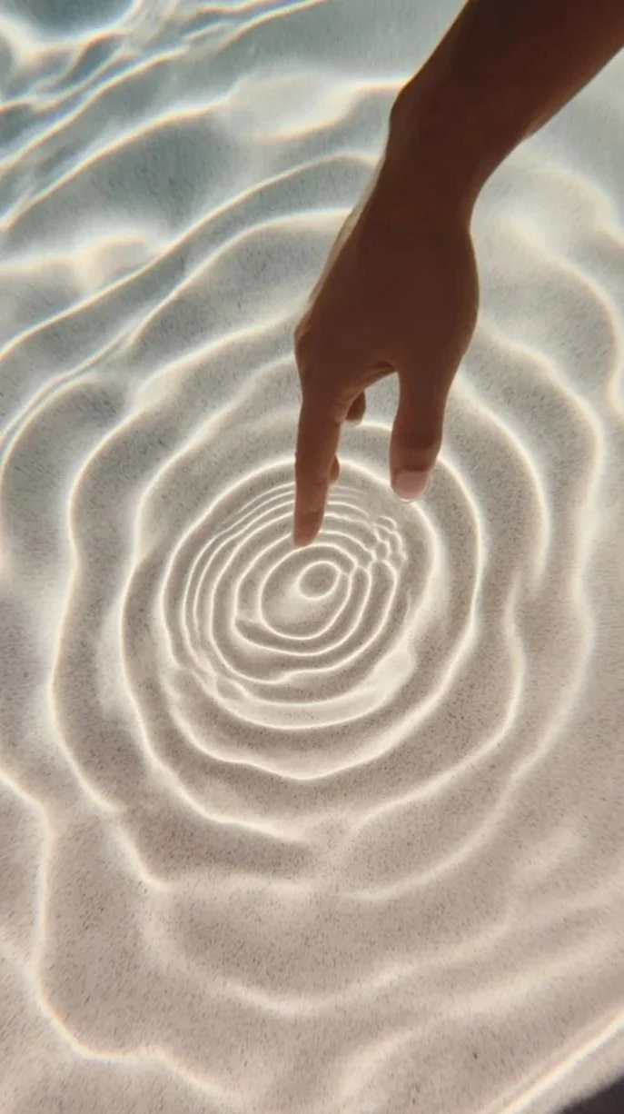 Person touching sandy water, creating ripples in the shallow water