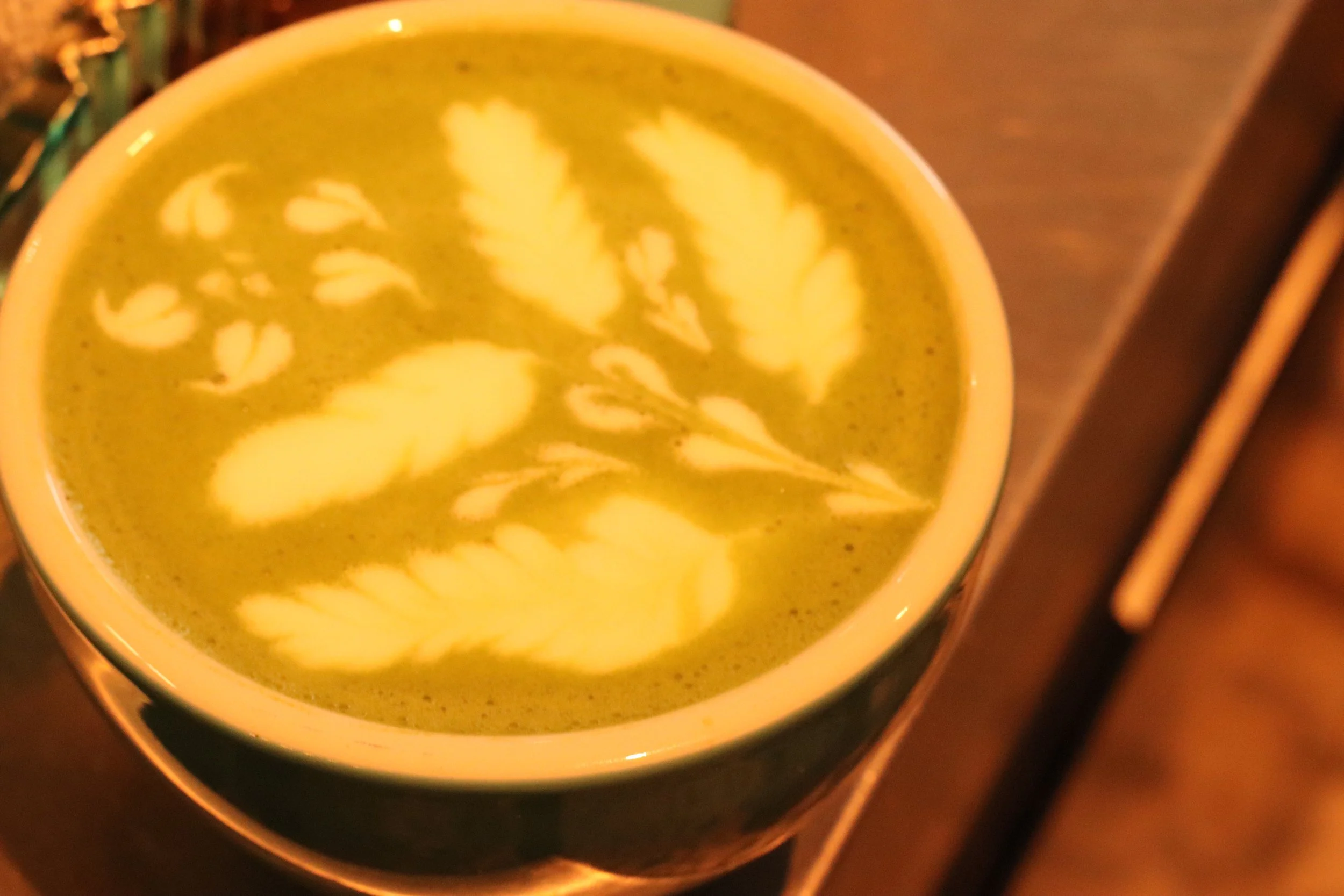 A mug of green tea with floral latte art on top, placed on a stove.