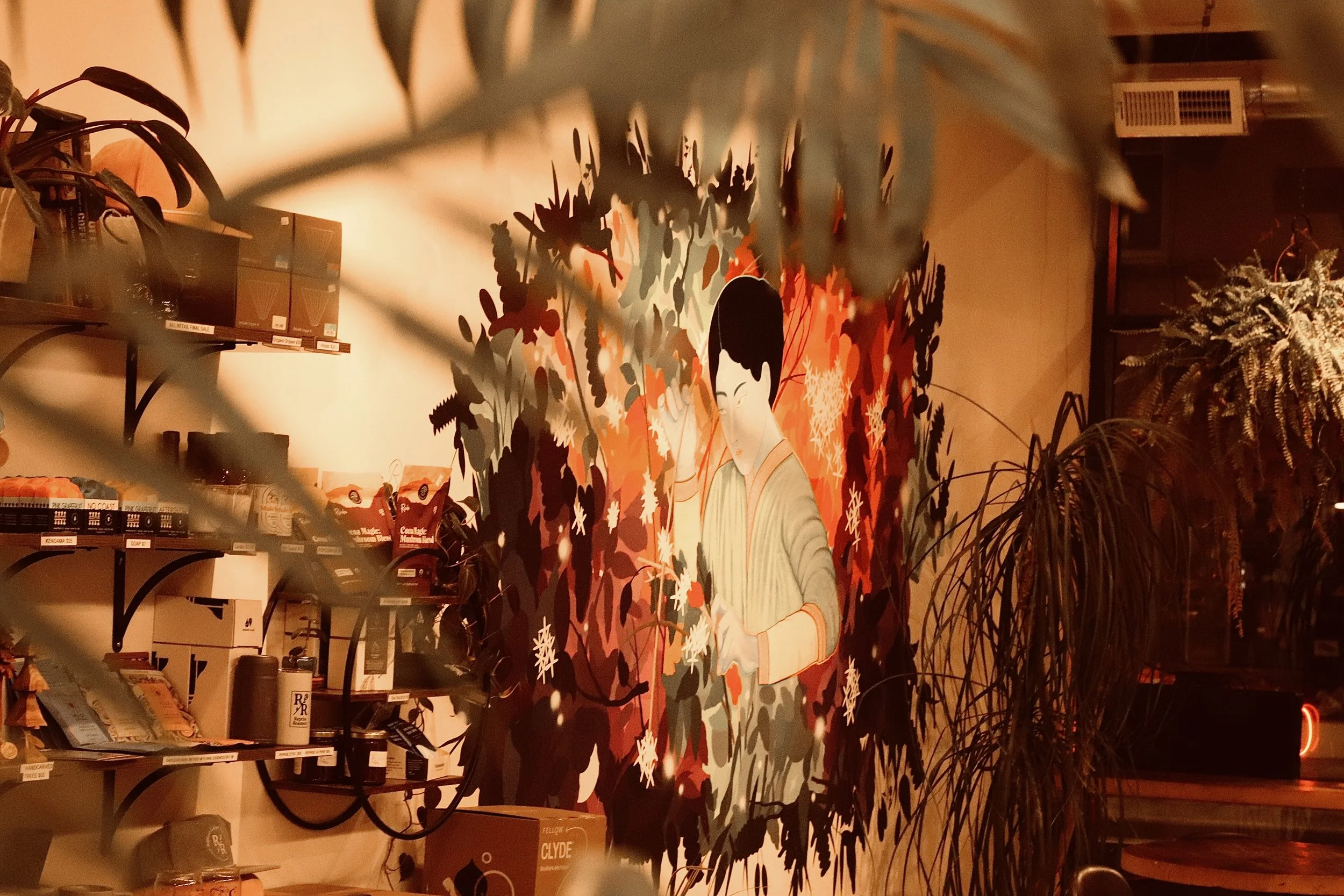 A colorful mural of a person with a traditional hairstyle surrounded by foliage. The scene appears to be in a retail store with shelves of products and plants visible in the background.