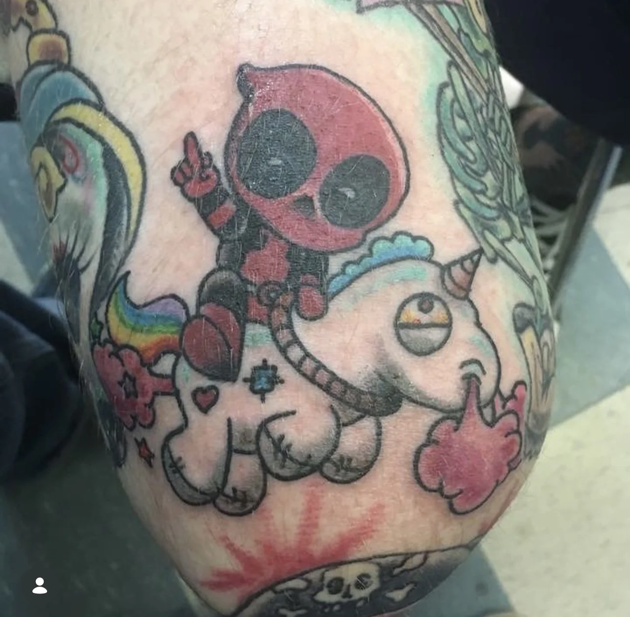 Tattoo of a cute cartoon spaceship with large eyes and a smile, holding a rainbow-colored cloud with stars and hearts around it.