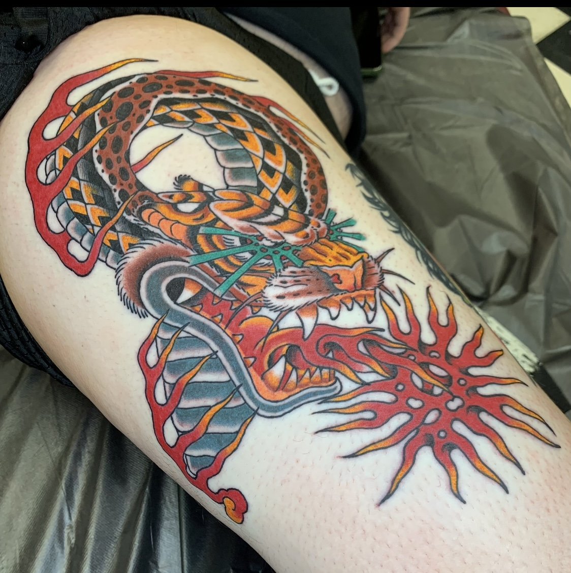 Colorful tattoo of a fierce tiger intertwined with a snake on a person's thigh.