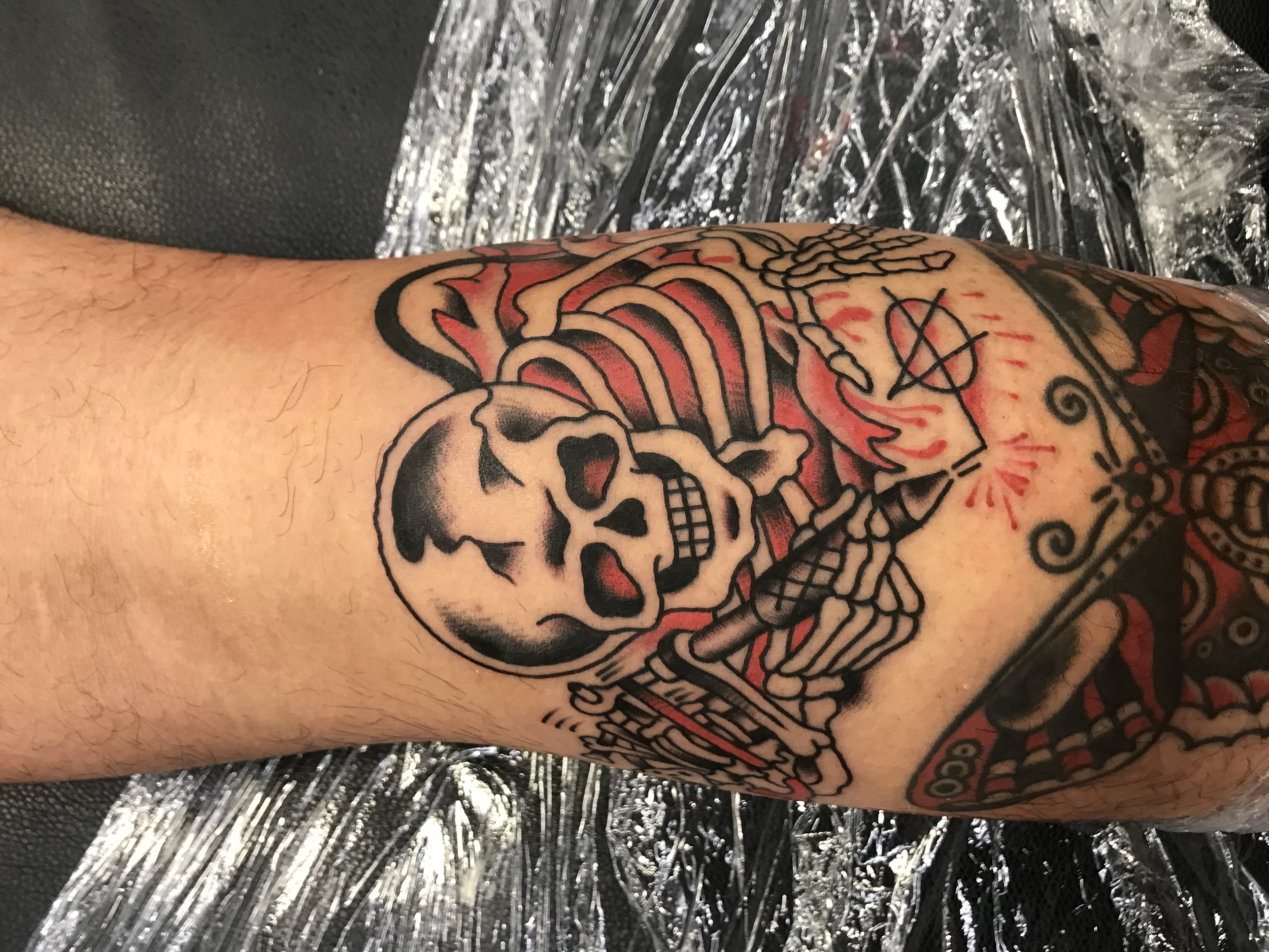 Close-up of a tattoo on a person's arm, featuring a skull and other designs in black and red ink.