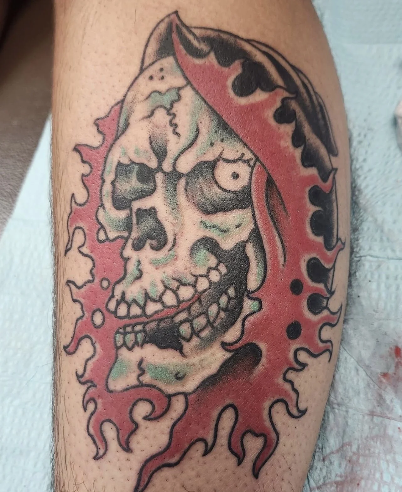 Tattoo of a skull with a red bandana on a person's upper arm, featuring bold black outlines and shading.