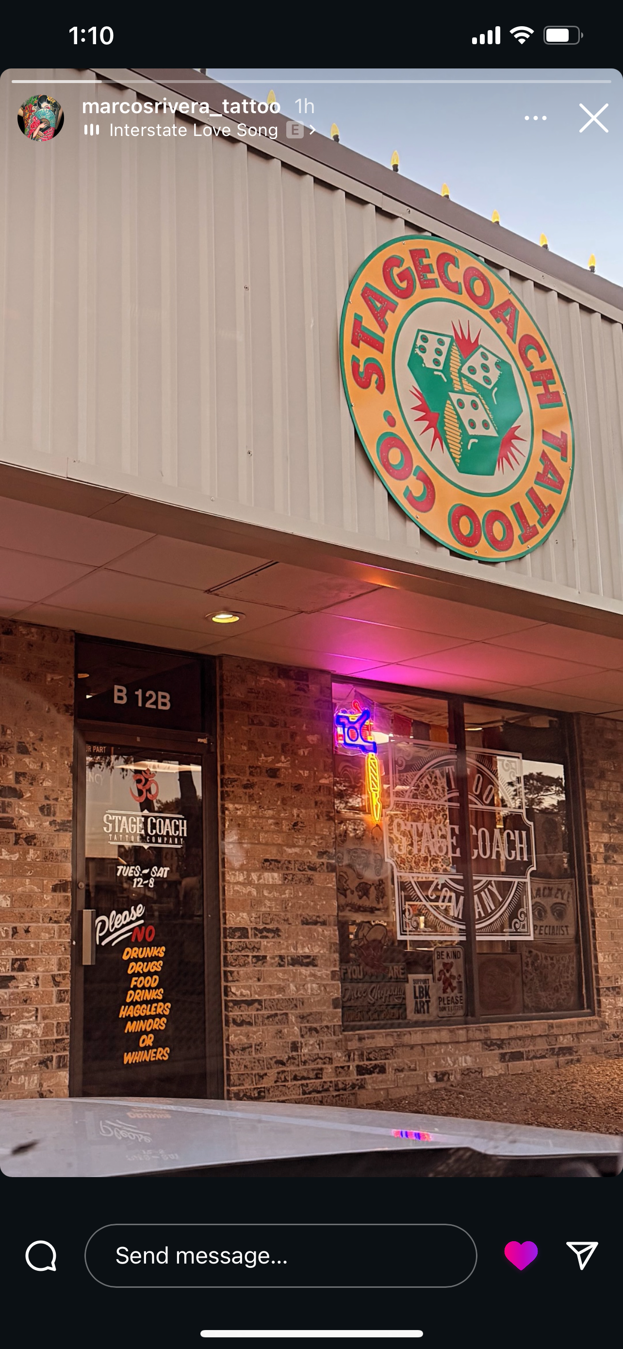 Exterior of a tattoo shop called Stage Coach with a large colorful sign featuring dice. The shop has a brick facade with neon signs on the window and a door displaying rules and hours.