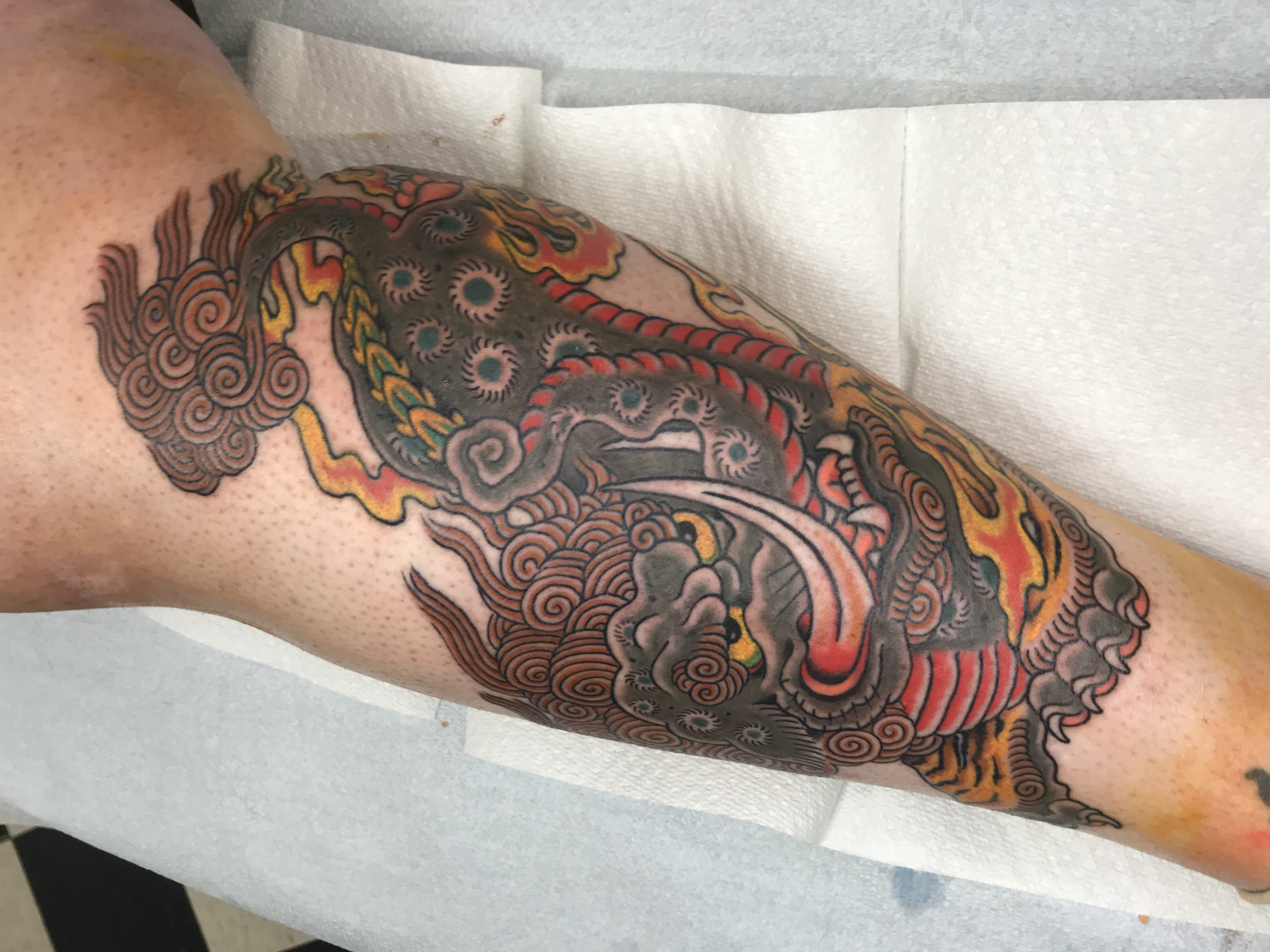 A detailed full sleeve tattoo featuring a multicolored mythical creature with swirling patterns, flames, and eye motifs on a person's arm. Japanese tattoo artists Lubbock,Tx Stagecoach Tattoo