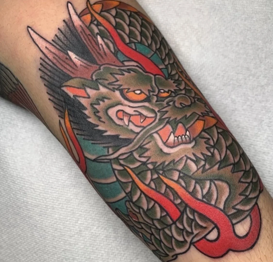 Colorful tattoo of a fierce dragon's head with sharp teeth, glowing eyes, and fiery accents on an arm.