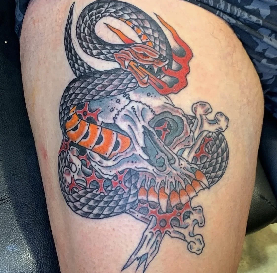 Tattoo of a snake wrapped around a skull and bones, with red and orange accents.
