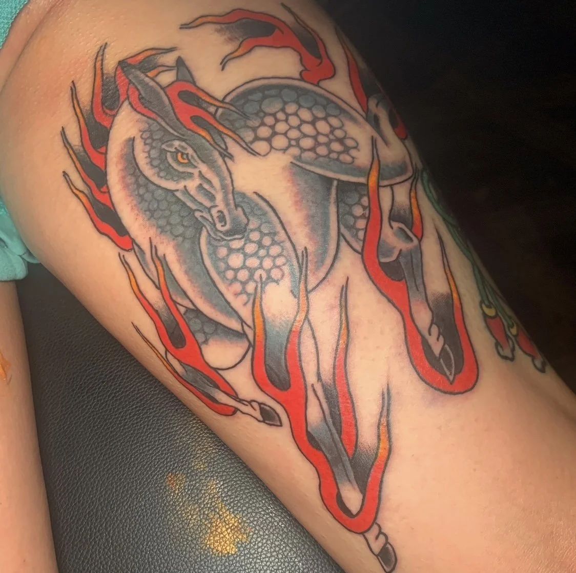 A detailed tattoo of a wolf with its head lowered, surrounded by red and orange flame-like designs, on a person's arm.