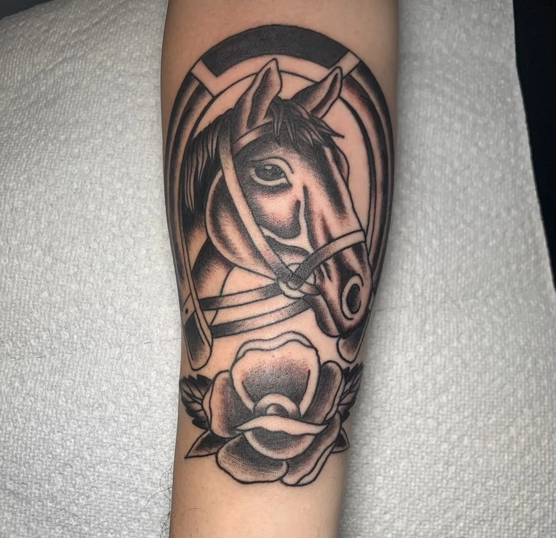Black and gray tattoo of a horse's head with a rose below it on a person's arm.