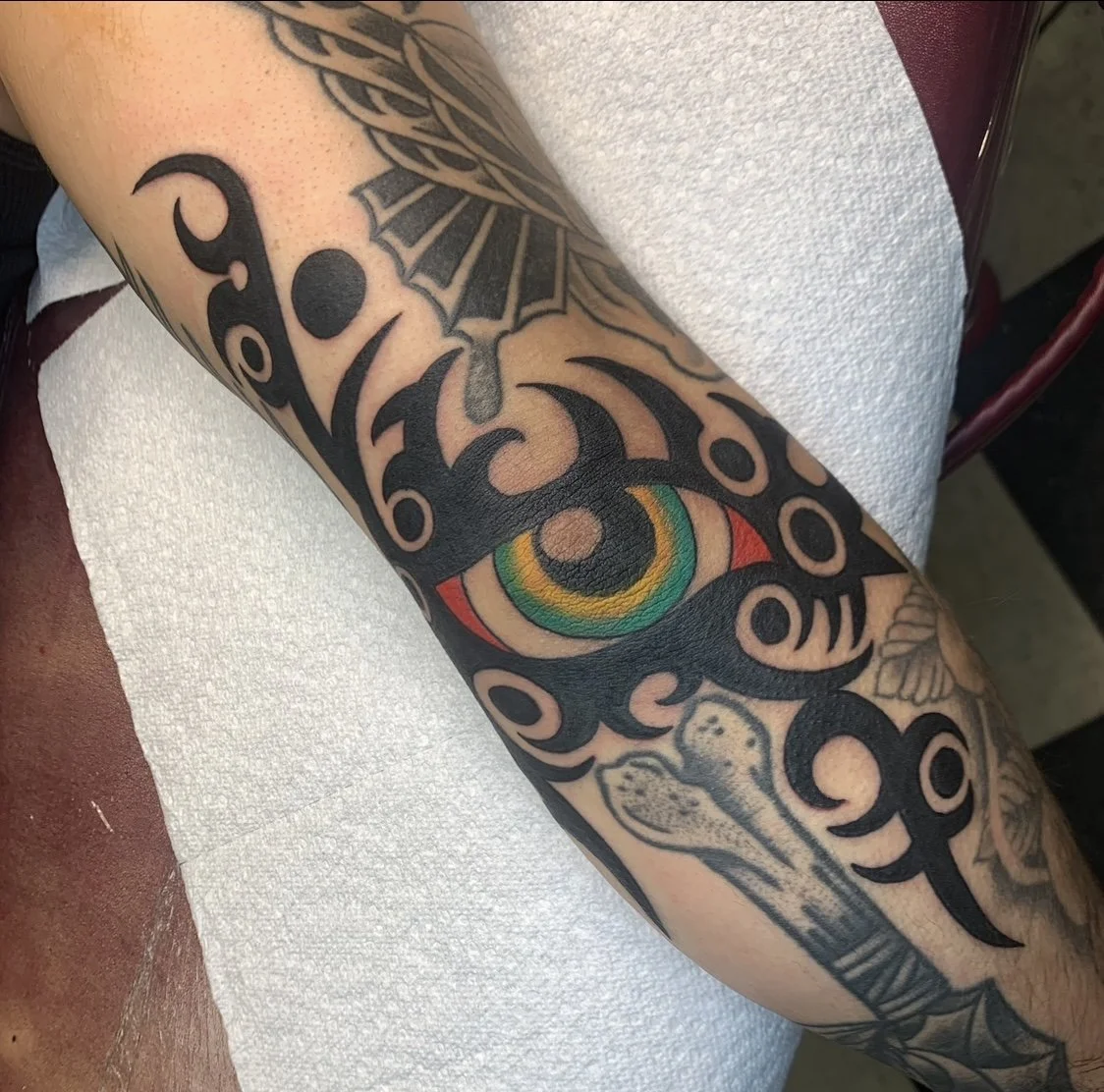 Tattoo sleeve with a colorful eye, tribal patterns, and other black ink designs on a person's arm.