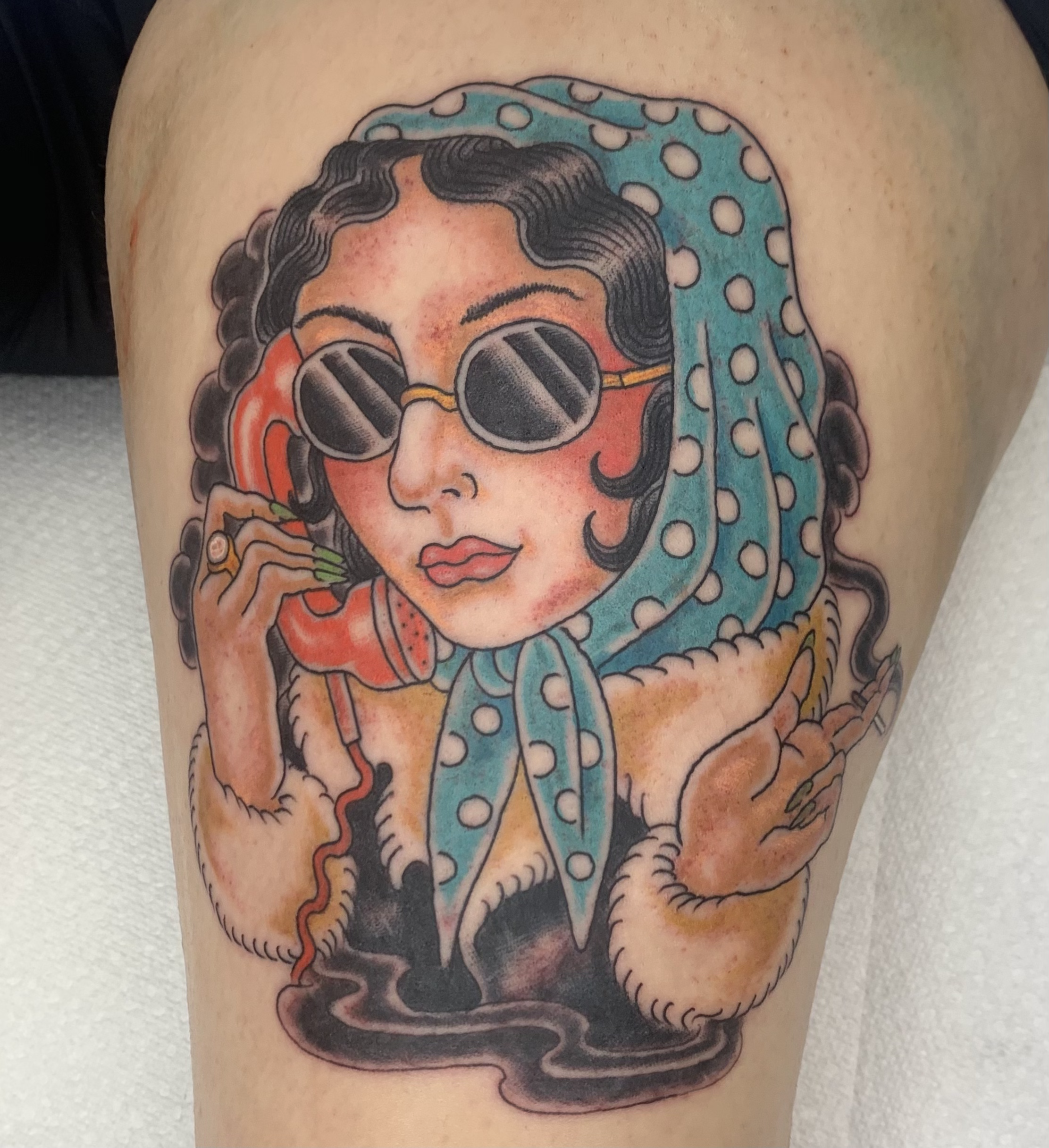 Tattoo of a woman with dark curly hair wearing sunglasses and a polka dot headscarf, holding a cigarette.