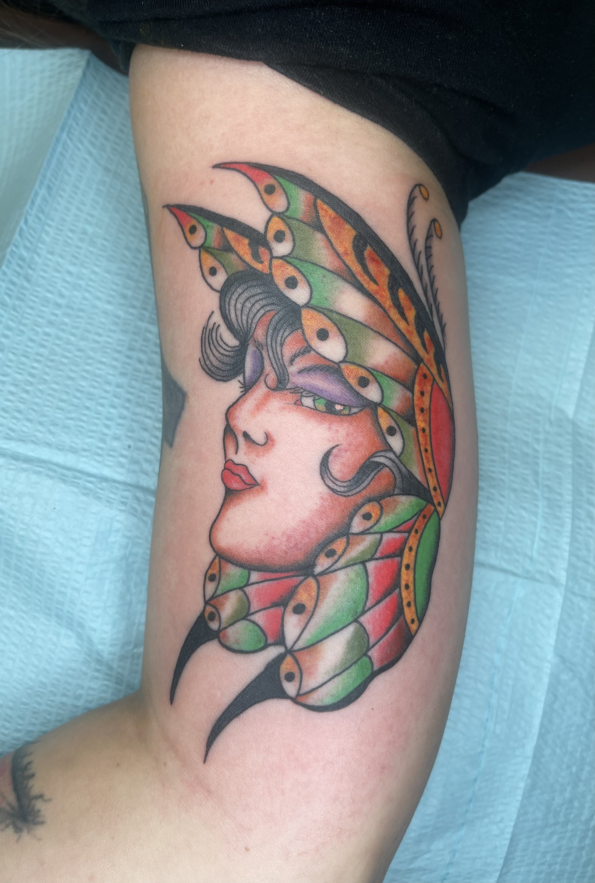 A colorful tattoo of a woman's face with butterfly wings in place of hair on a person's upper arm.