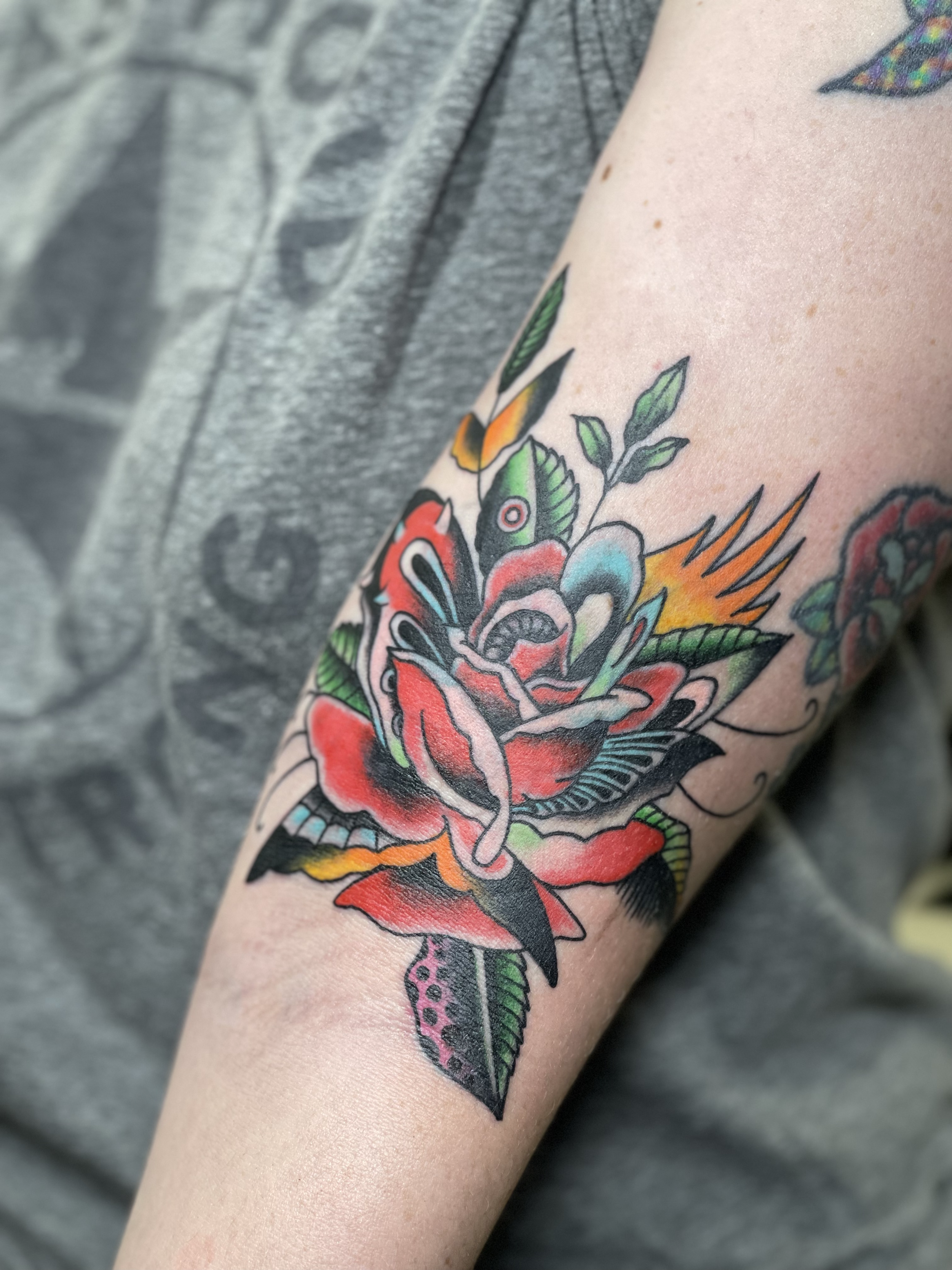 Colorful tattoo of a rose and leaves on a person's arm.