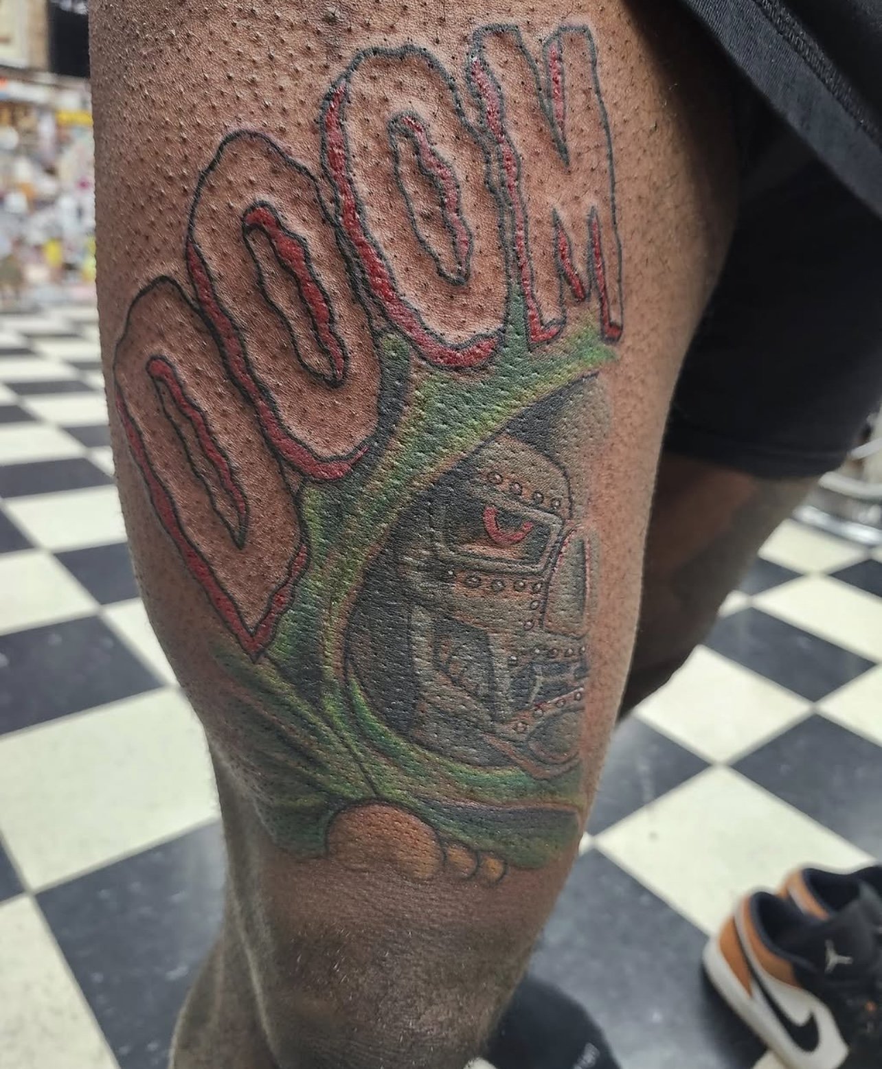 Colorful tattoo on person's leg featuring a tree with the word 'POON' in flower-like letters and a stylized rocket ship and planets below.