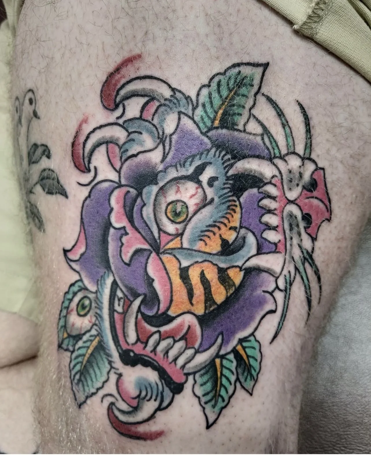 Colorful tattoo of a tiger's face with floral and leaf motifs on person's skin.
