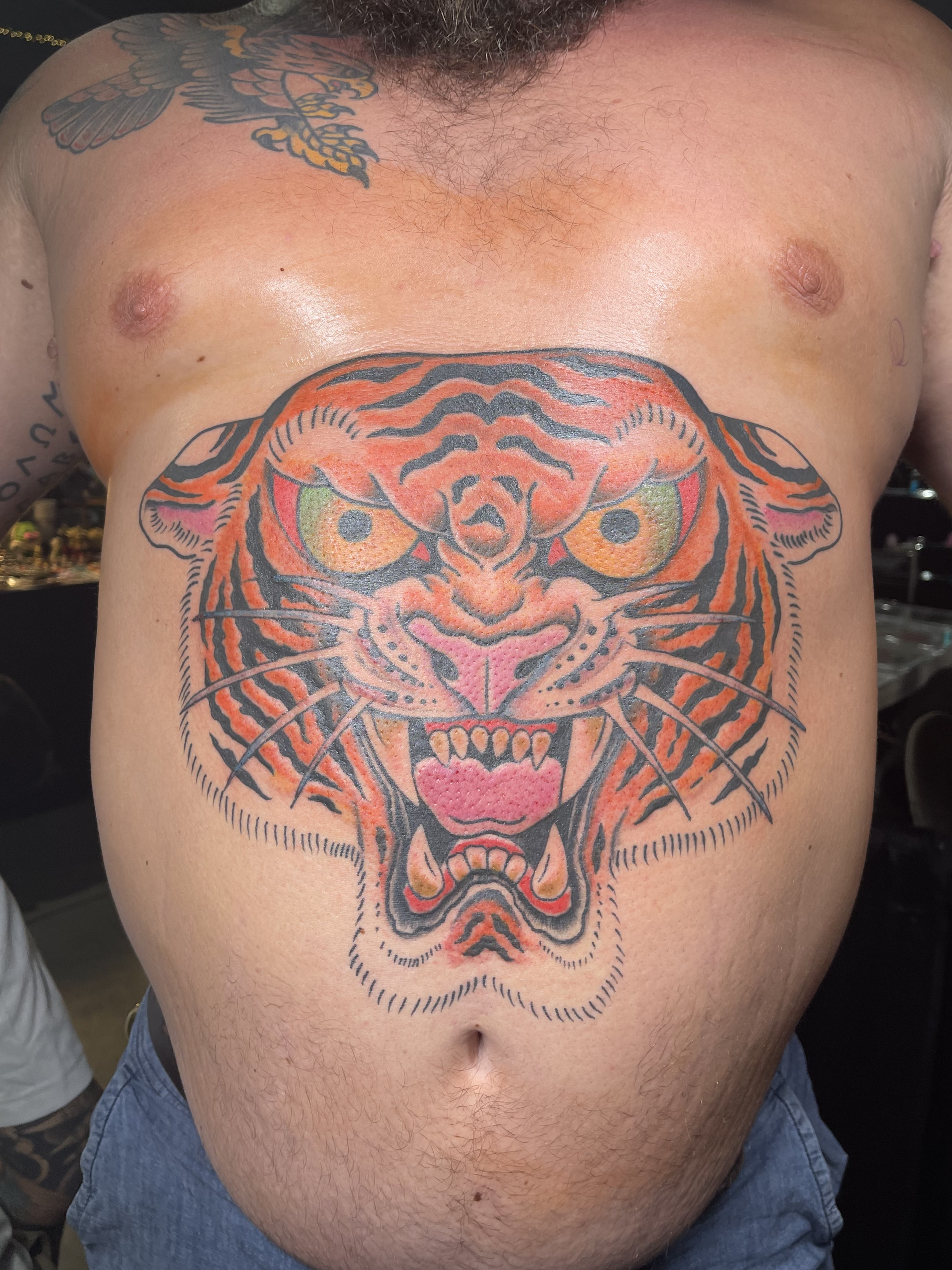 Tattoo of a fierce tiger's face covering the person's chest, with bright orange, black, yellow, and green details.