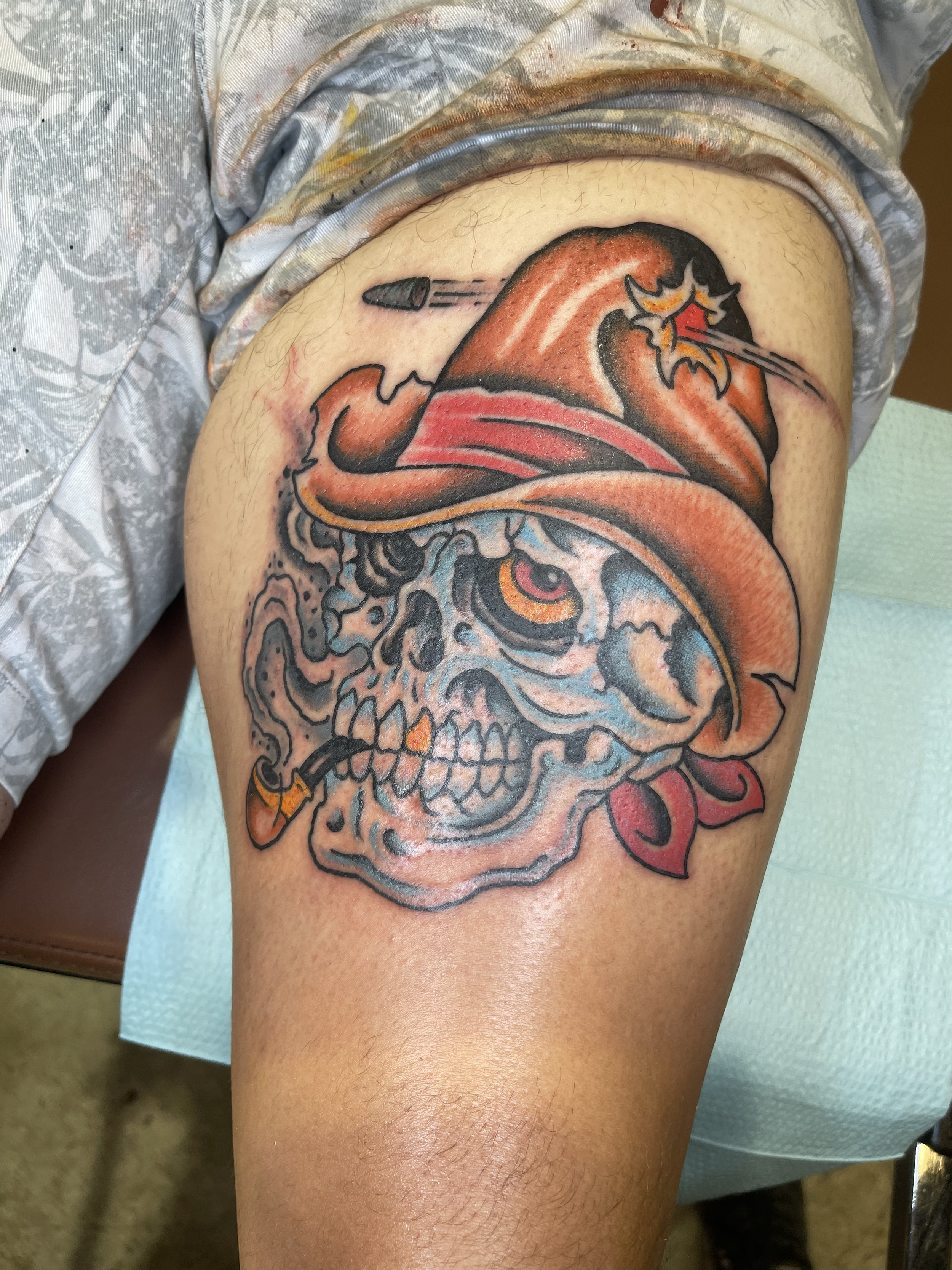 A colorful tattoo of a skull with a design resembling a Japanese demon mask, featuring red, black, and orange hues, located on a person's upper arm.