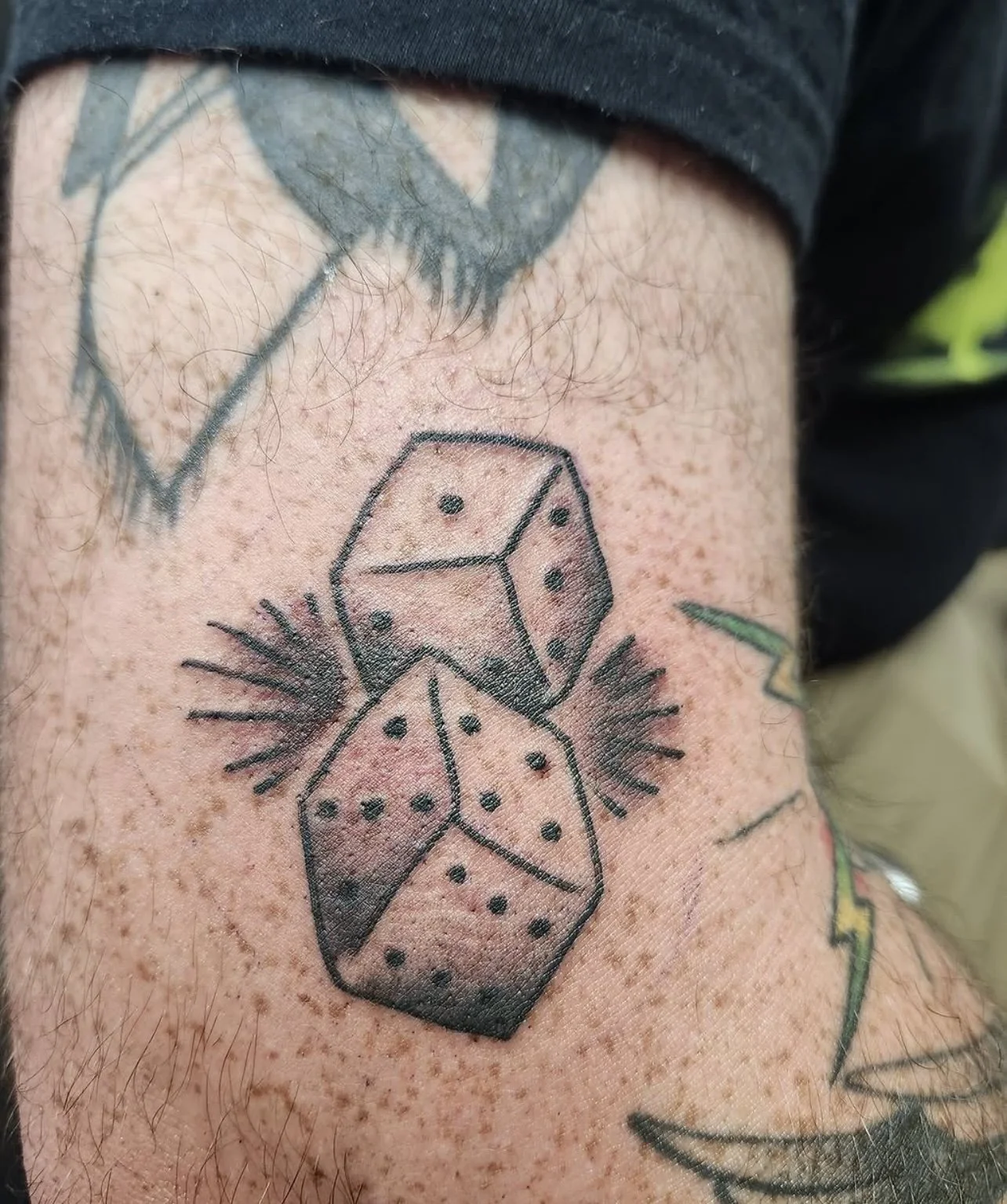 Tattoo of three dice arranged vertically with small lines radiating outward, on a person's arm with visible hair and skin.