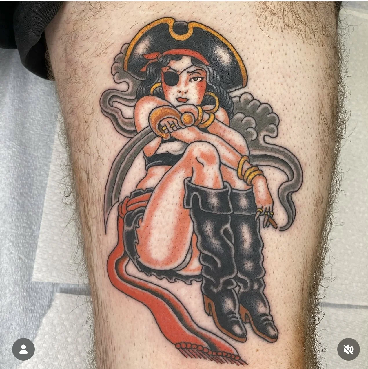Tattoo of a pirate woman with an eyepatch, holding a sword, wearing black boots, jewelry, and a hat, with a smoking pipe and waves in the background.