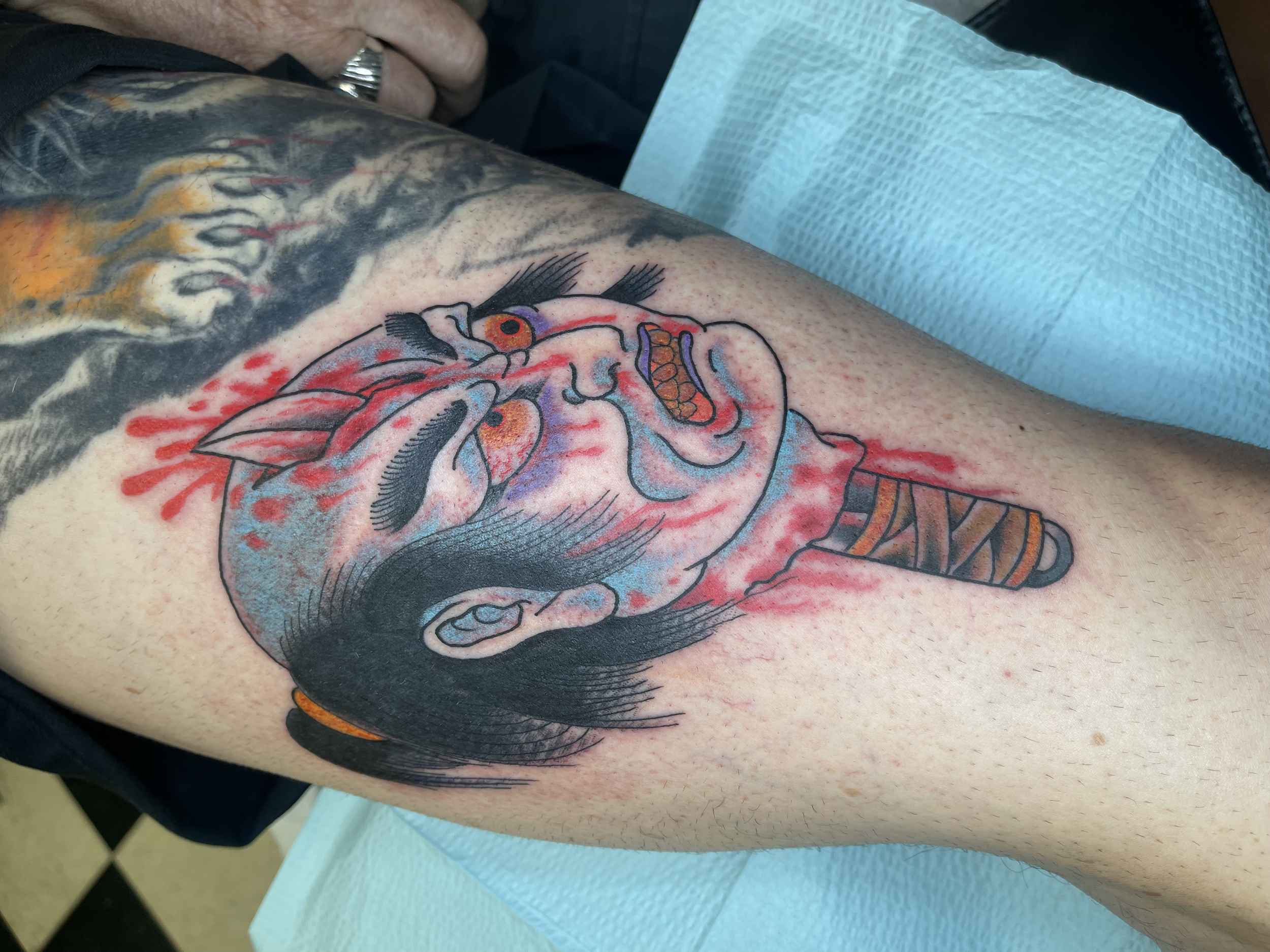 Colorful tattoo of a bird with an orange eye, black feathers, blue and purple accents, and a pink beak on a person's upper arm.