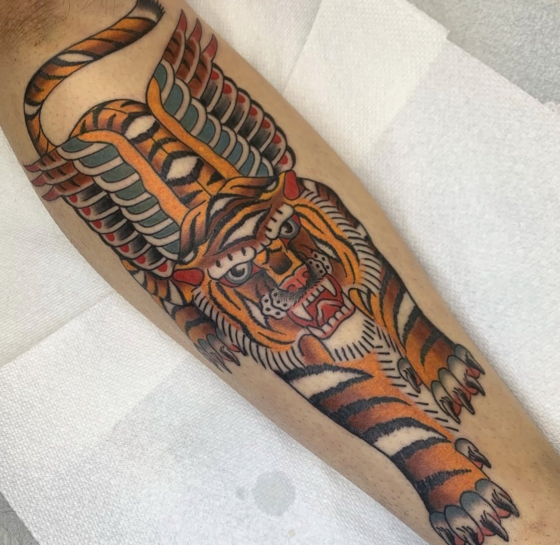 Colorful traditional tiger tattoo on person's arm with detailed stripes and fierce expression.