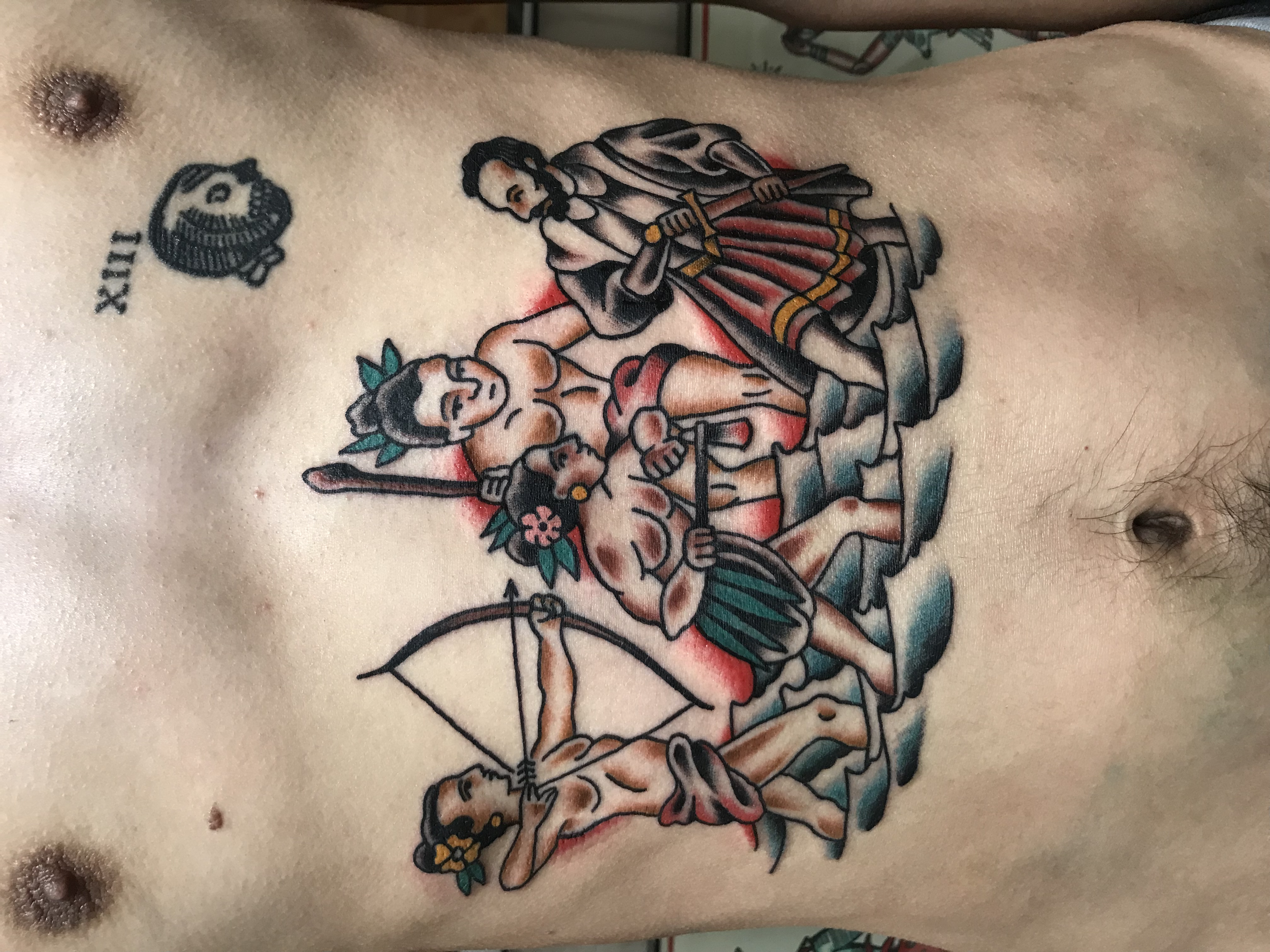 A tattoo on a person's chest featuring a woman's face with flowers, two men in traditional clothing holding guns, and a landscape background.