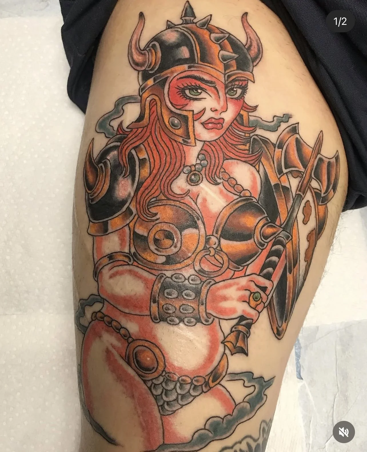 Tattoo of a female warrior with a horned helmet, armor, and a spear, depicted in a colorful, illustrative style on a person's thigh.