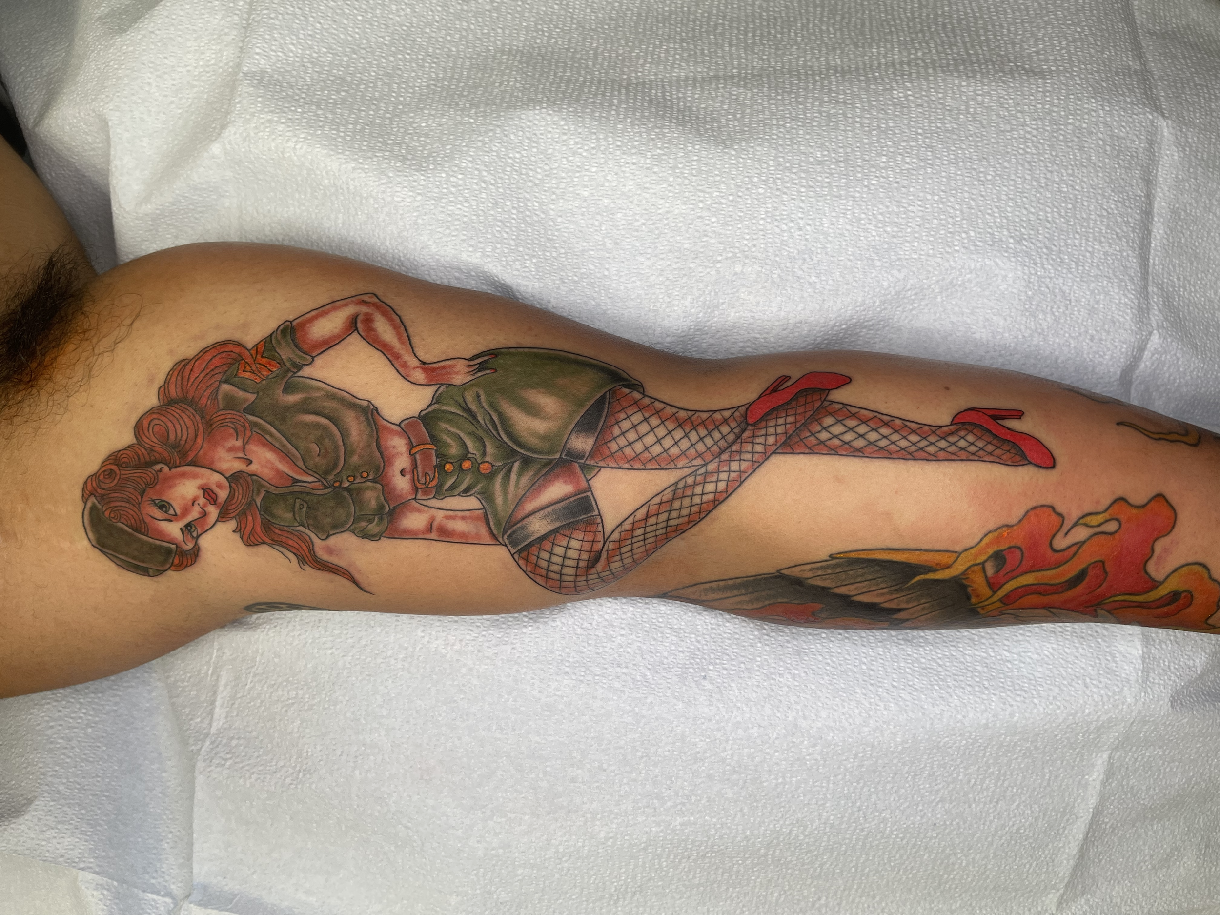 Colorful tattoo of a pin-up girl with red hair, fishnet stockings, and military clothing on a person's arm.